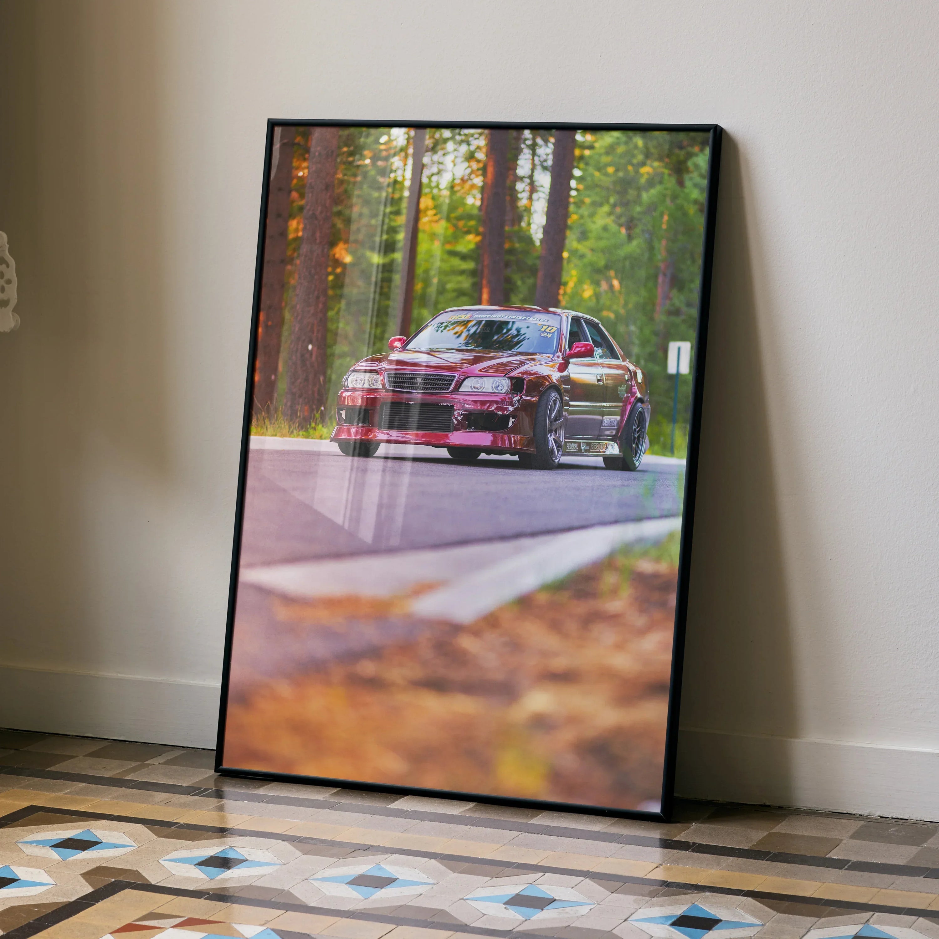Toyota Chaser JDM drift car poster with black frame leaning against a wall, autumn forest background.