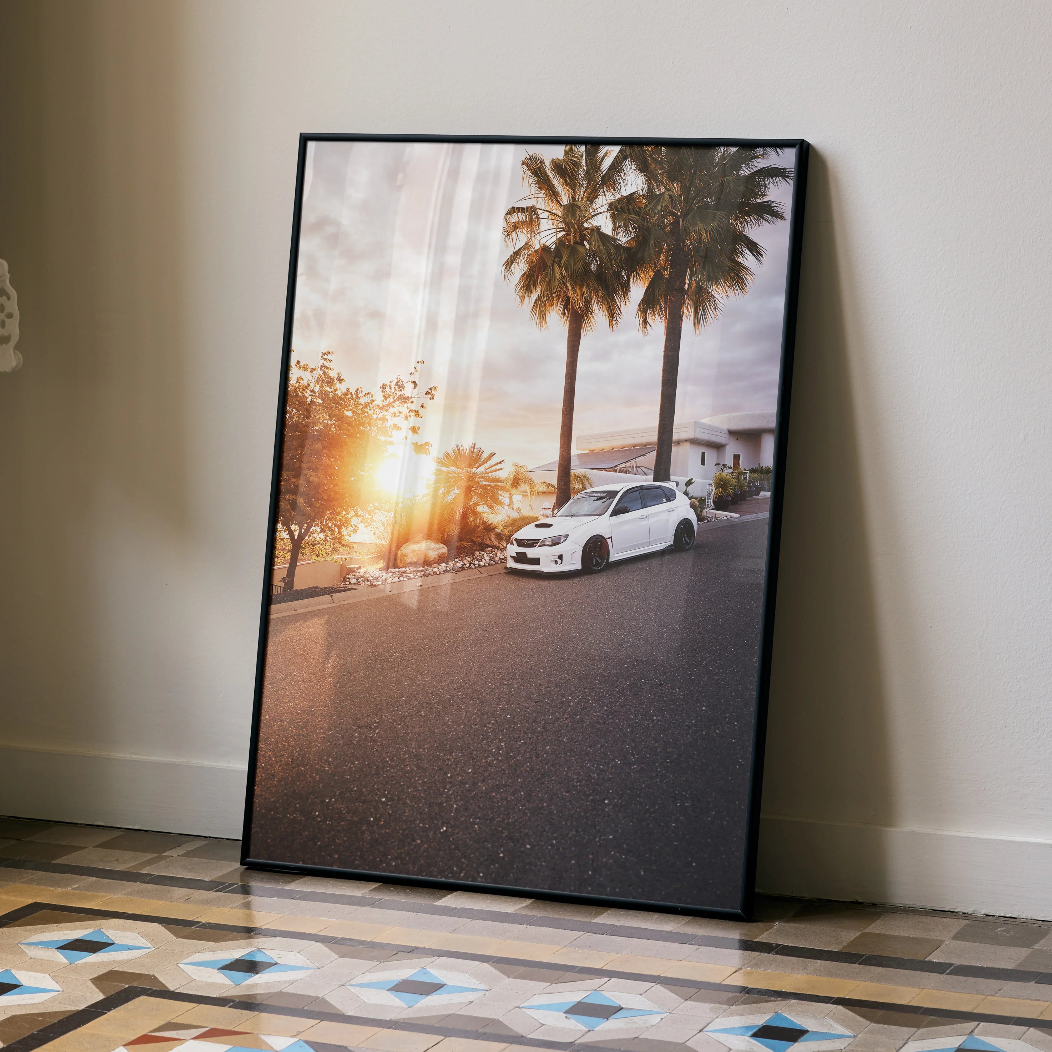 Sunset Subaru WRX STI poster wall art with palm trees in black frame, leaning on floor.