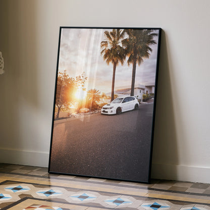 Sunset Subaru WRX STI poster wall art with palm trees in black frame, leaning on floor.