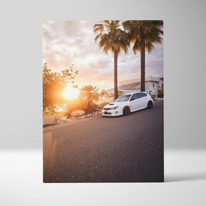Vertical canvas wall art featuring a white Subaru WRX STI parked by palm trees at sunset.