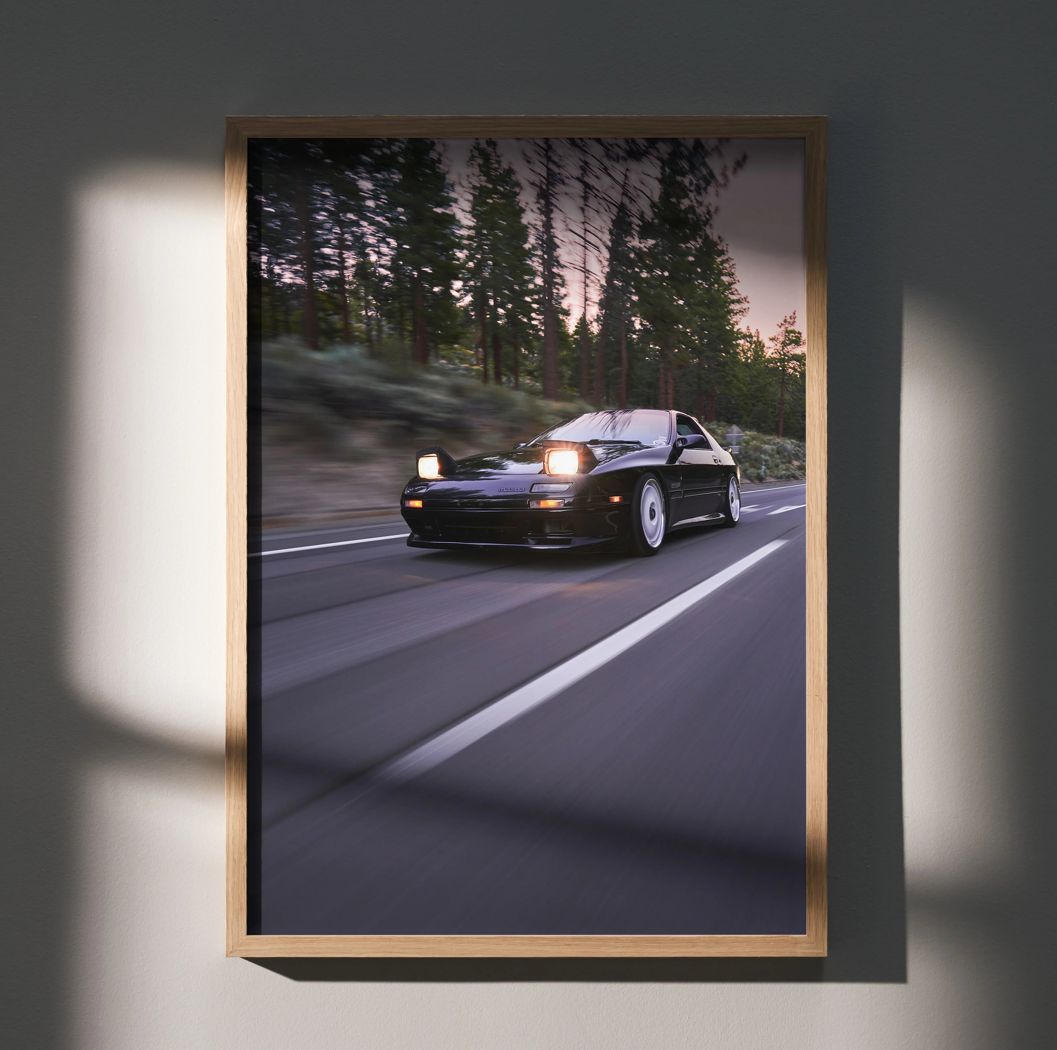 Mazda FC RX7 driving on forest road at dusk poster wall art in wooden frame.