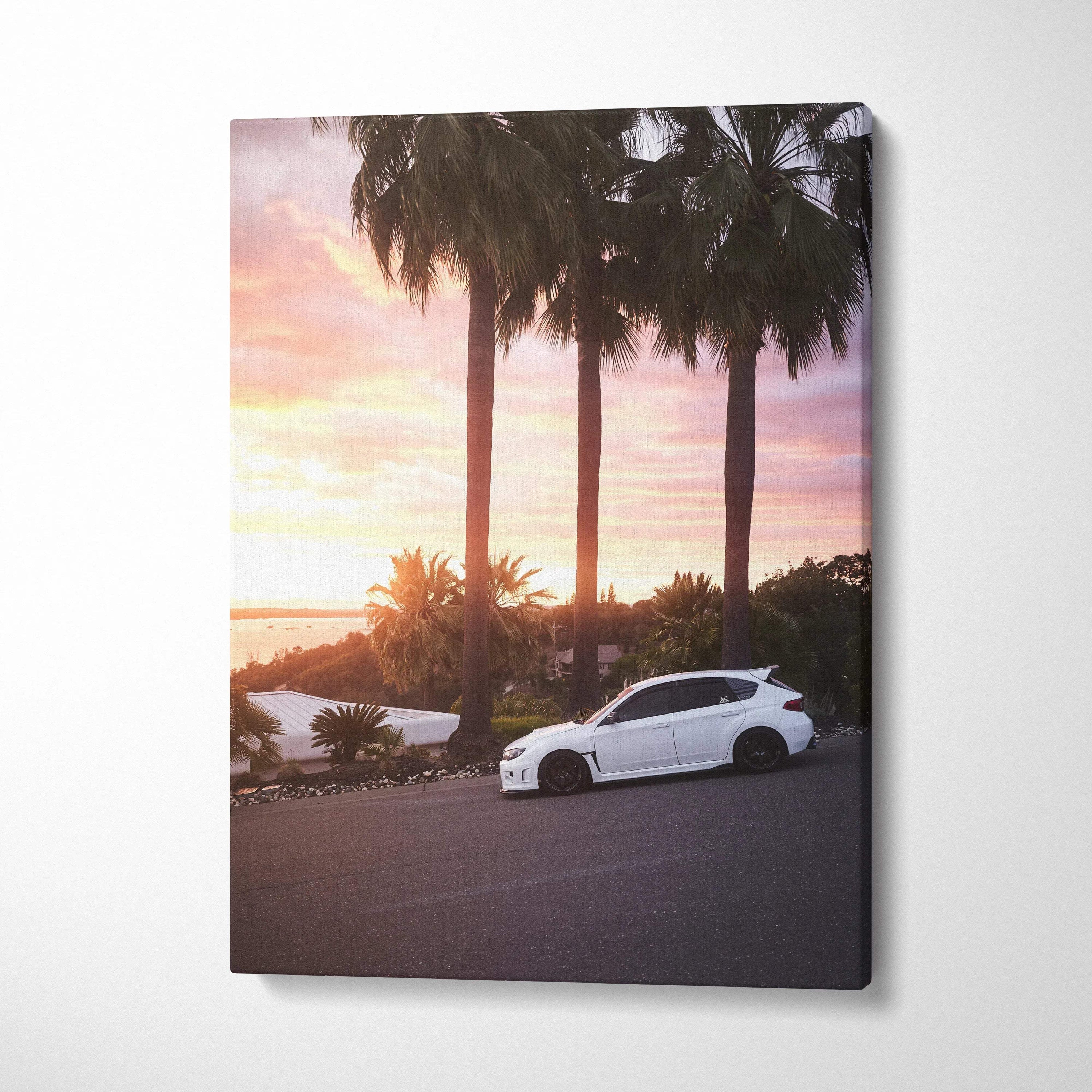 Vertical canvas wall art of white Subaru WRX STI parked by palm trees at sunset with vibrant sky colors.