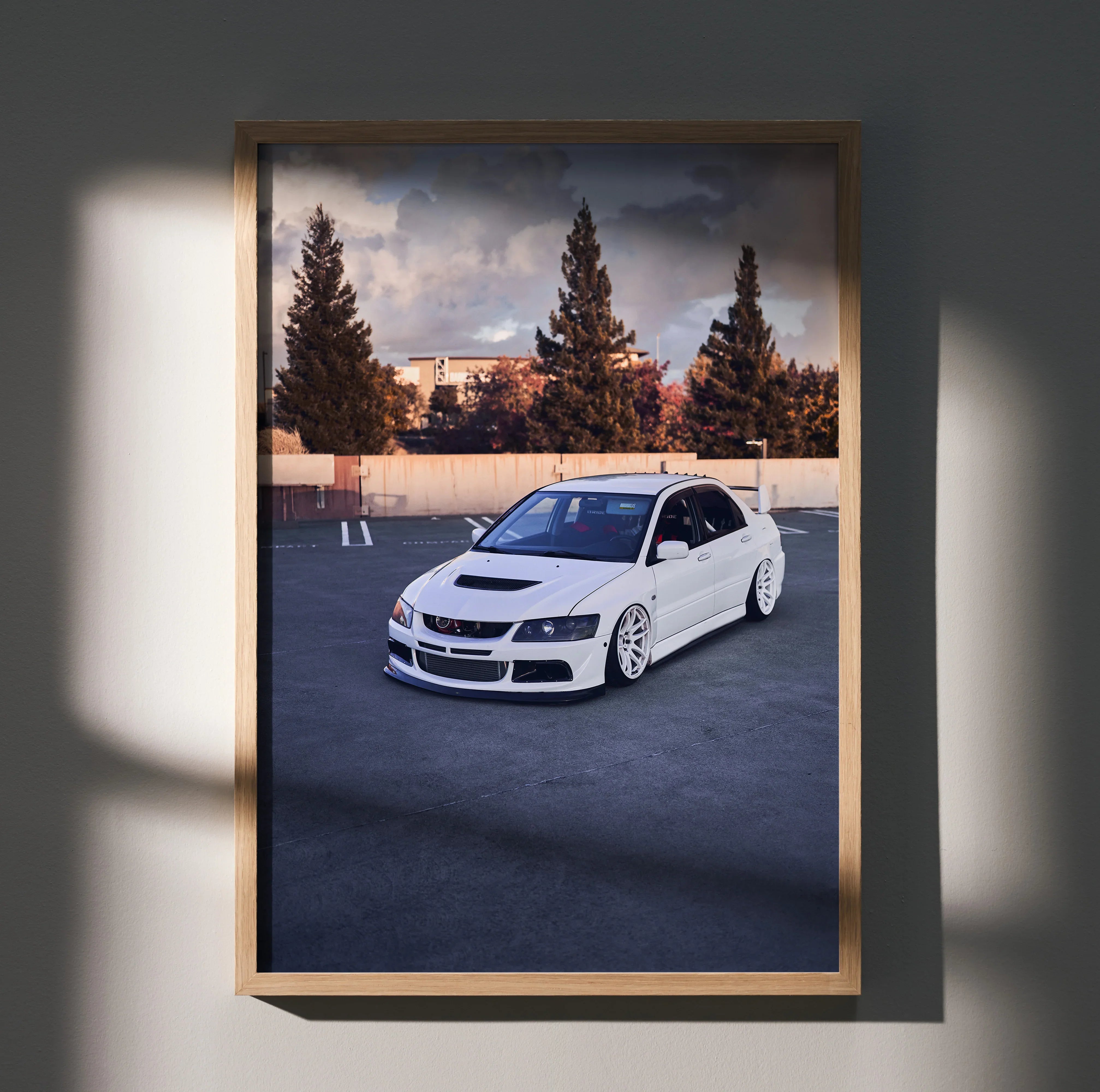 White Mitsubishi Evo 8 parked in empty lot with trees and building background poster wall art.