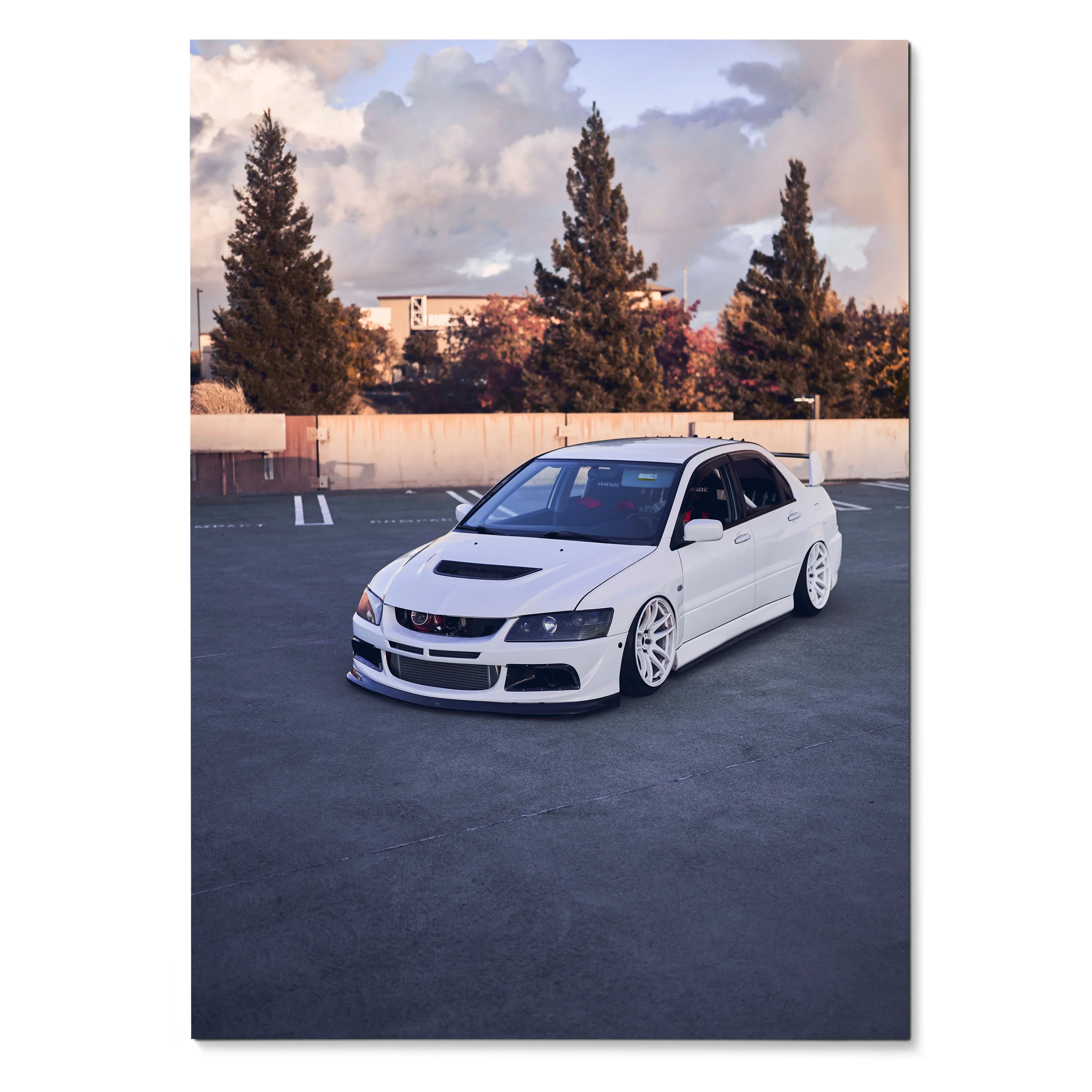White Mitsubishi Evo 8 lowered in parking lot with tall trees and cloudy sky poster wall art.