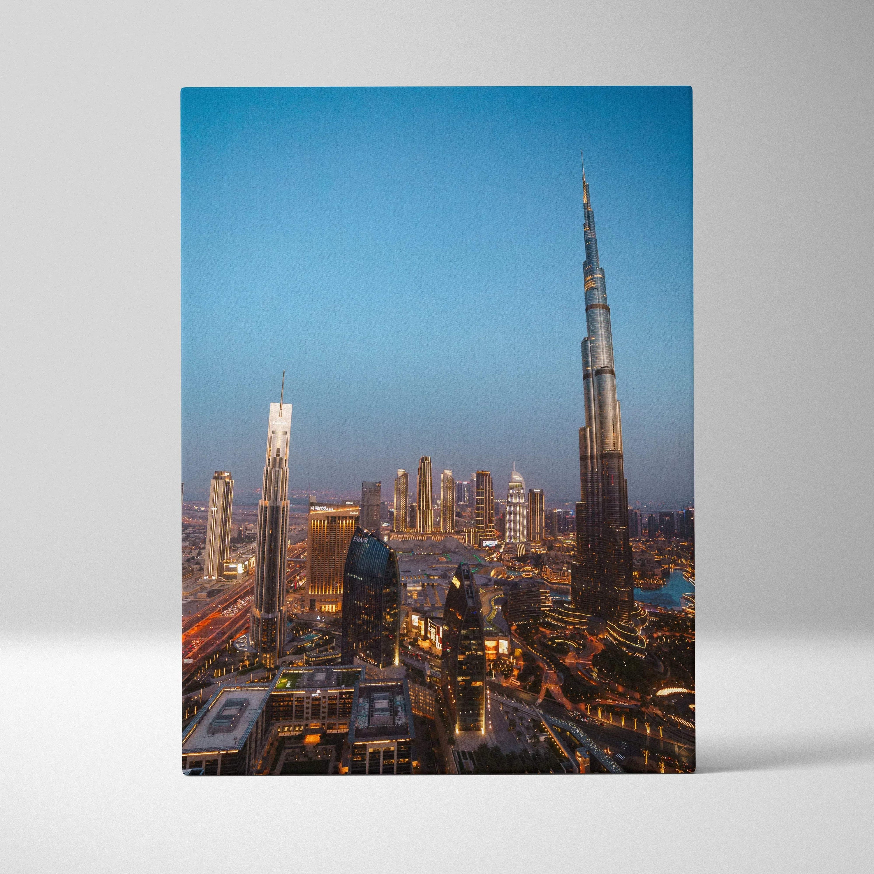 Vertical canvas wall art featuring illuminated modern skyscrapers at dusk with a clear blue sky backdrop.