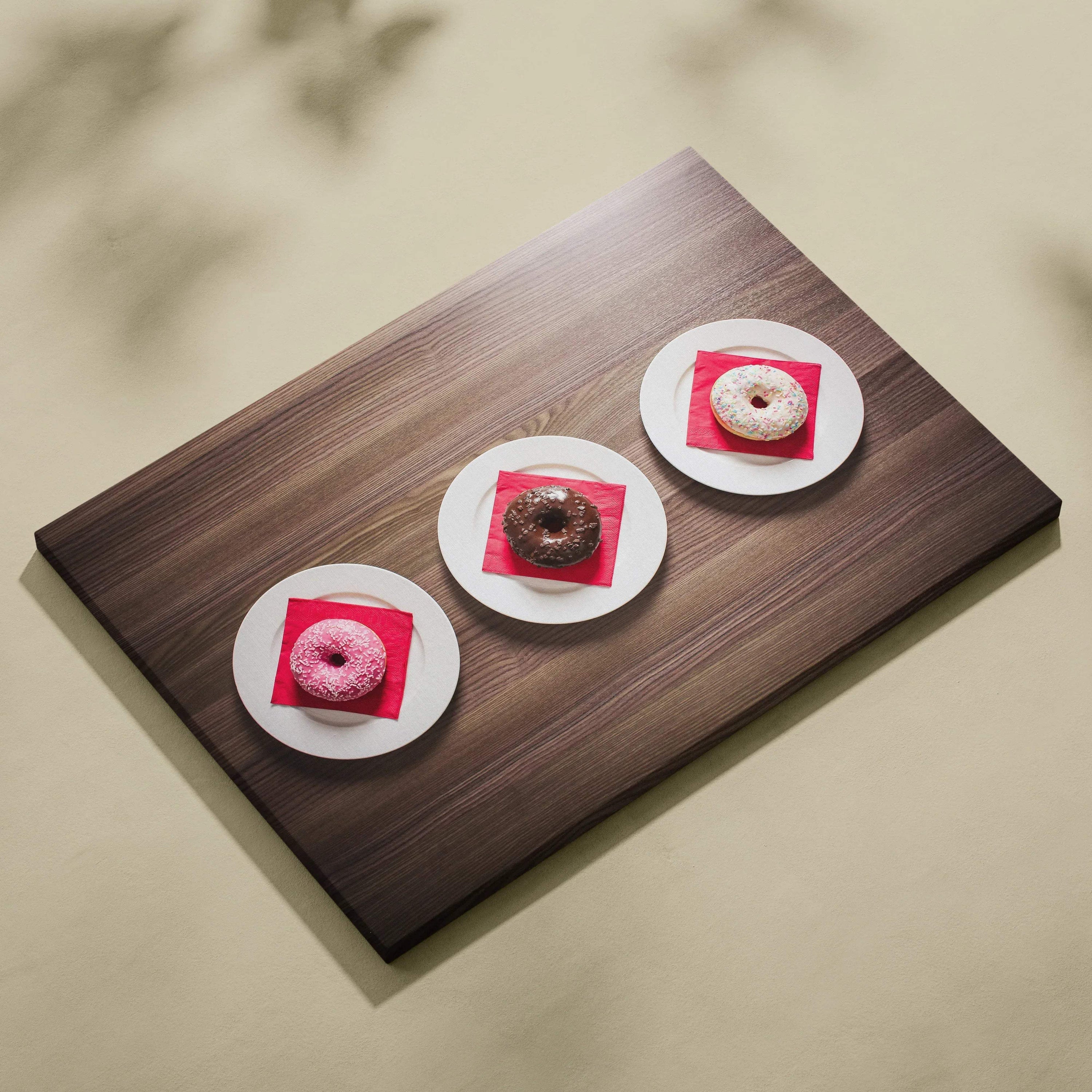 Canvas wall art print featuring three colorful glazed donuts on white plates against a wooden surface background.