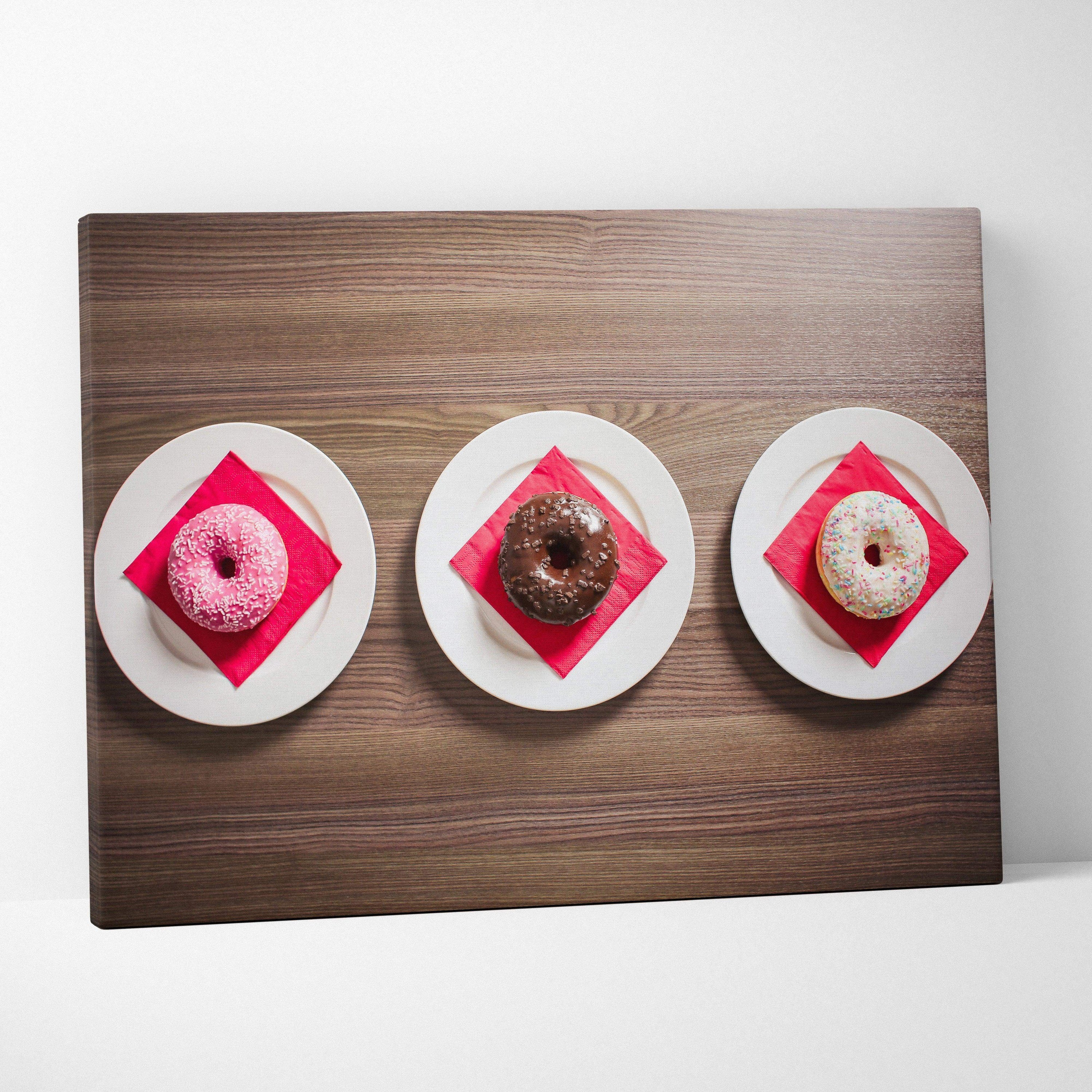 Canvas wall art featuring three glazed donuts—pink, chocolate, and white with sprinkles—each on white plates with red.