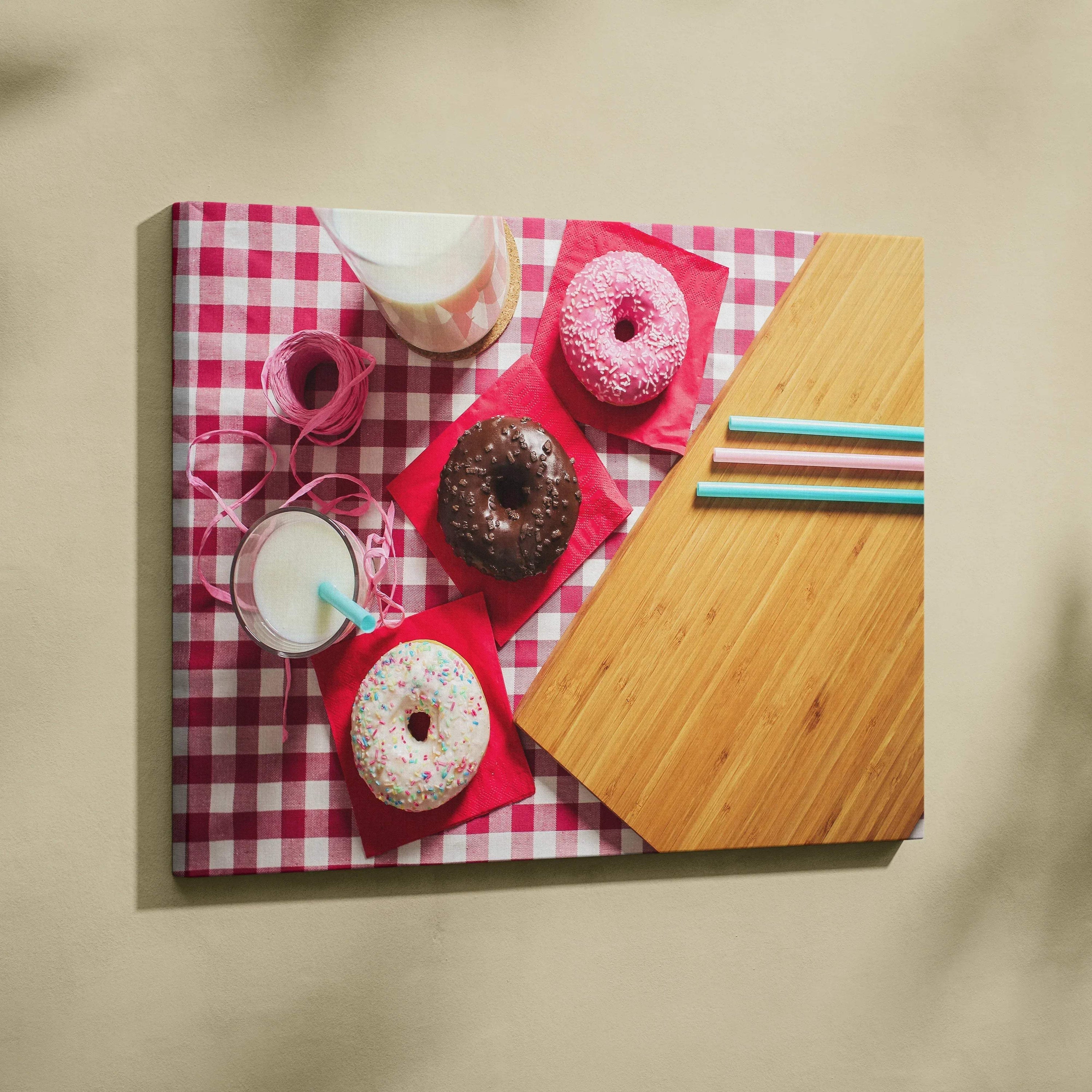 Colorful donut-themed canvas wall art with sprinkles on a pink checkered background and wooden table decor.