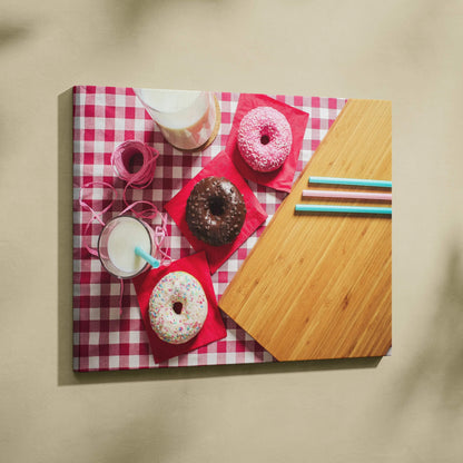 Colorful donut-themed canvas wall art with sprinkles on a pink checkered background and wooden table decor.