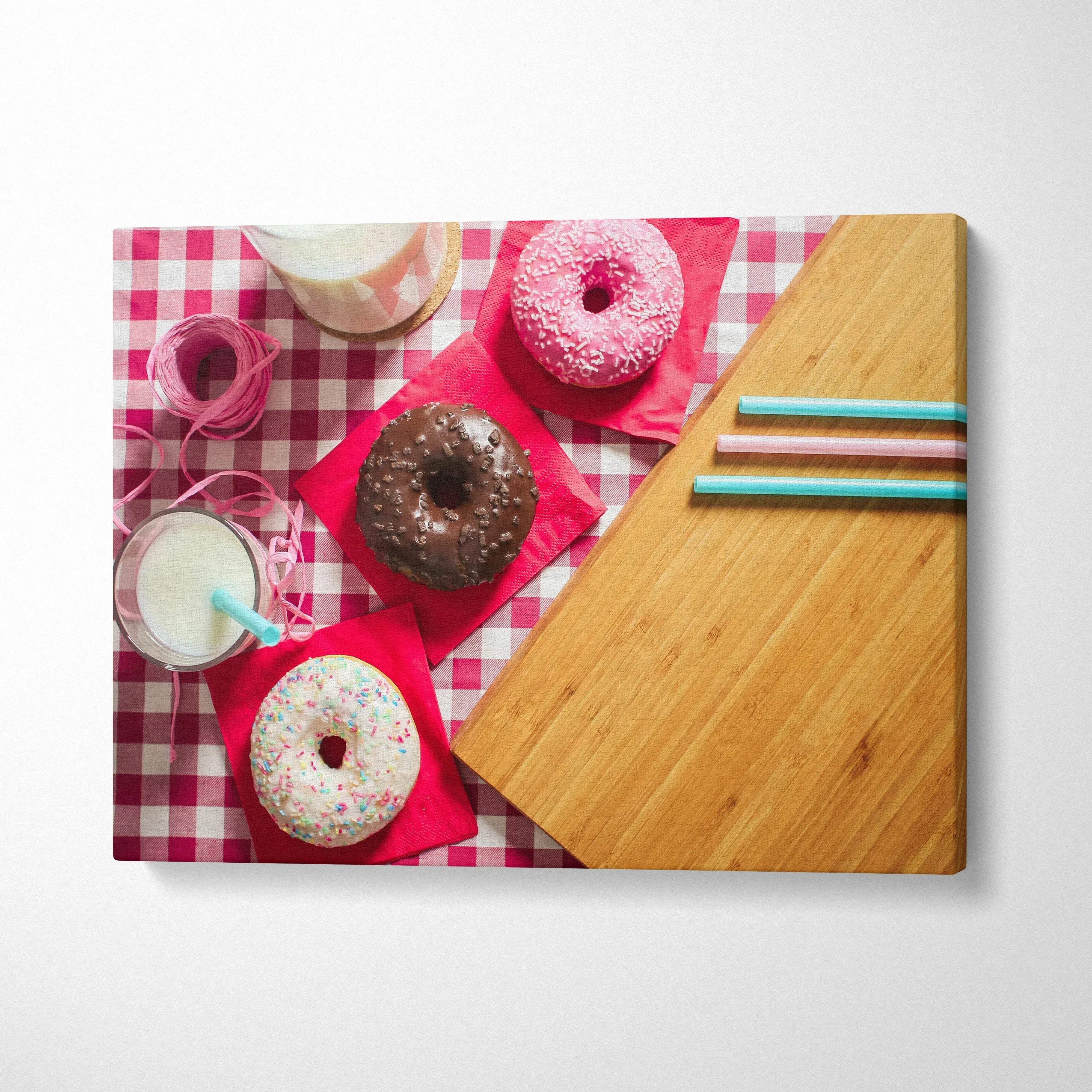 Canvas wall art featuring colorful donuts with sprinkles on red napkins over pink gingham tablecloth with milk and straws,.