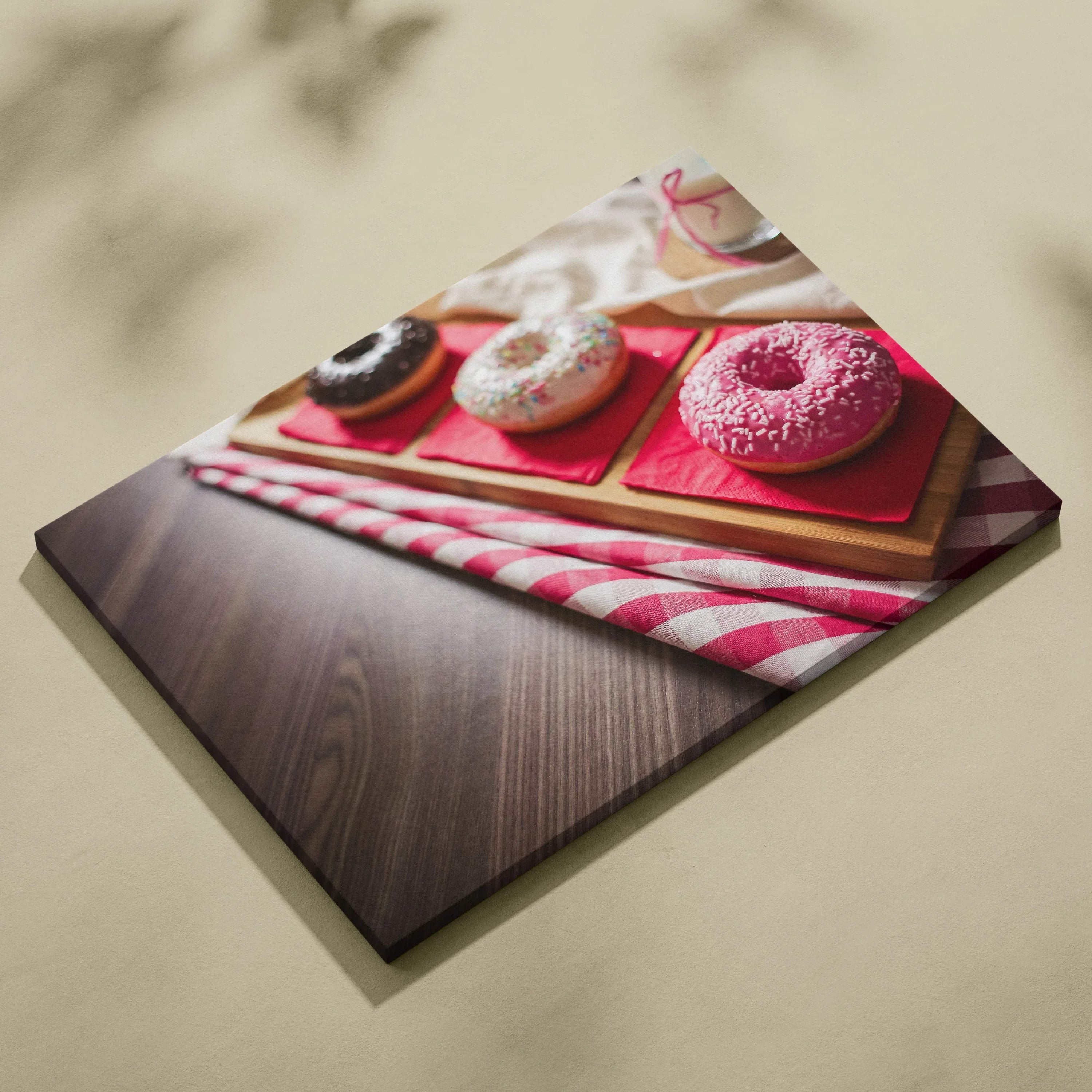 Canvas wall art featuring three glazed donuts in pink, white, and chocolate on wooden trays with a red and white striped.