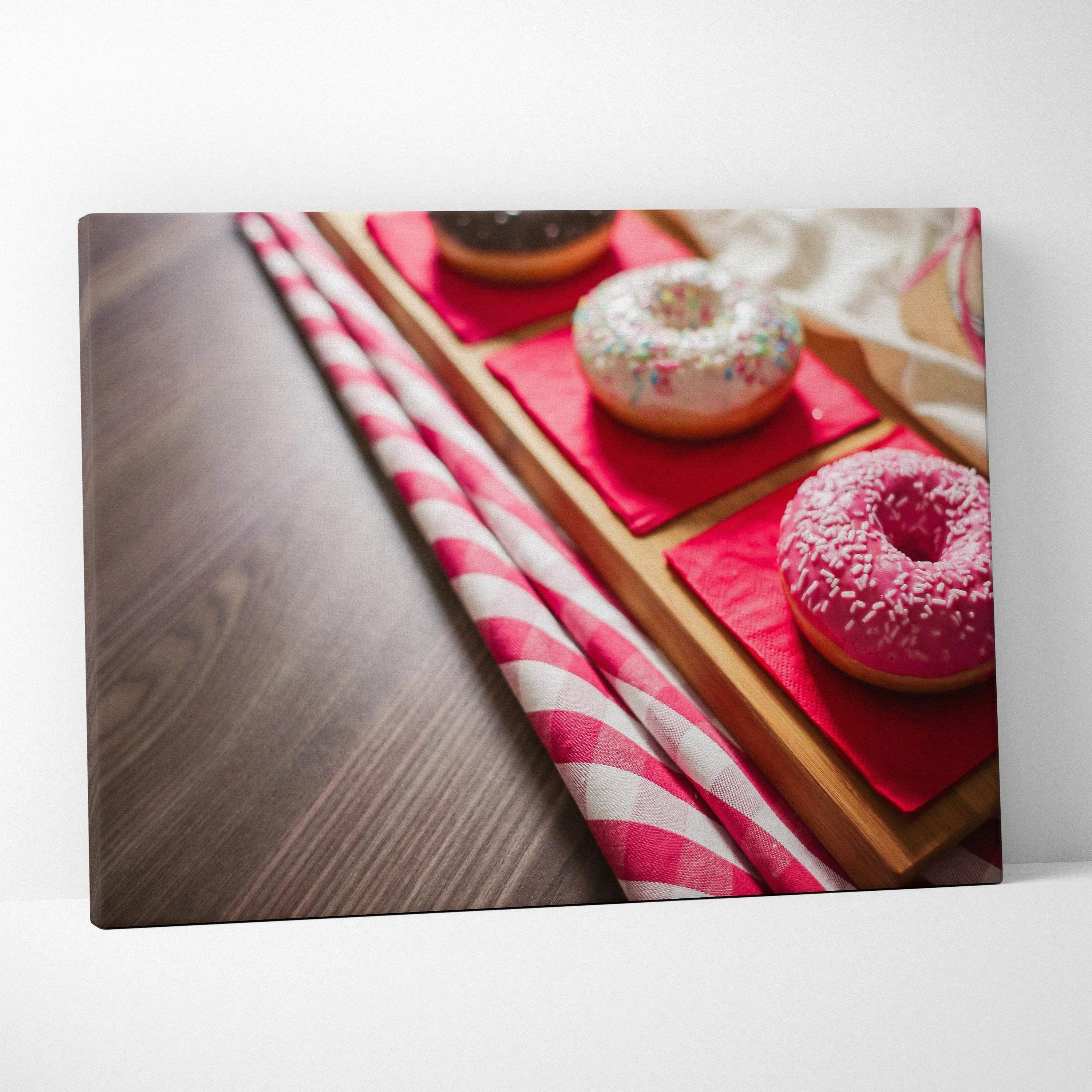 Vibrant canvas wall art featuring three glazed donuts with colorful sprinkles on red napkins, displayed on a wooden surface.