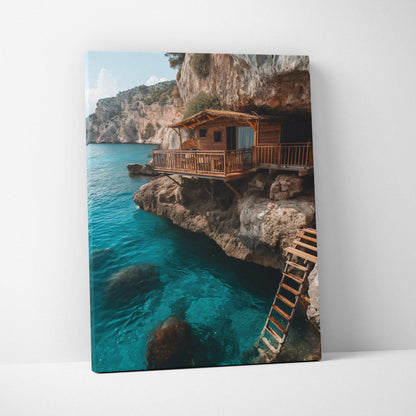 Canvas wall art featuring a rustic wooden cabin perched on rocky cliffs above clear blue water.
