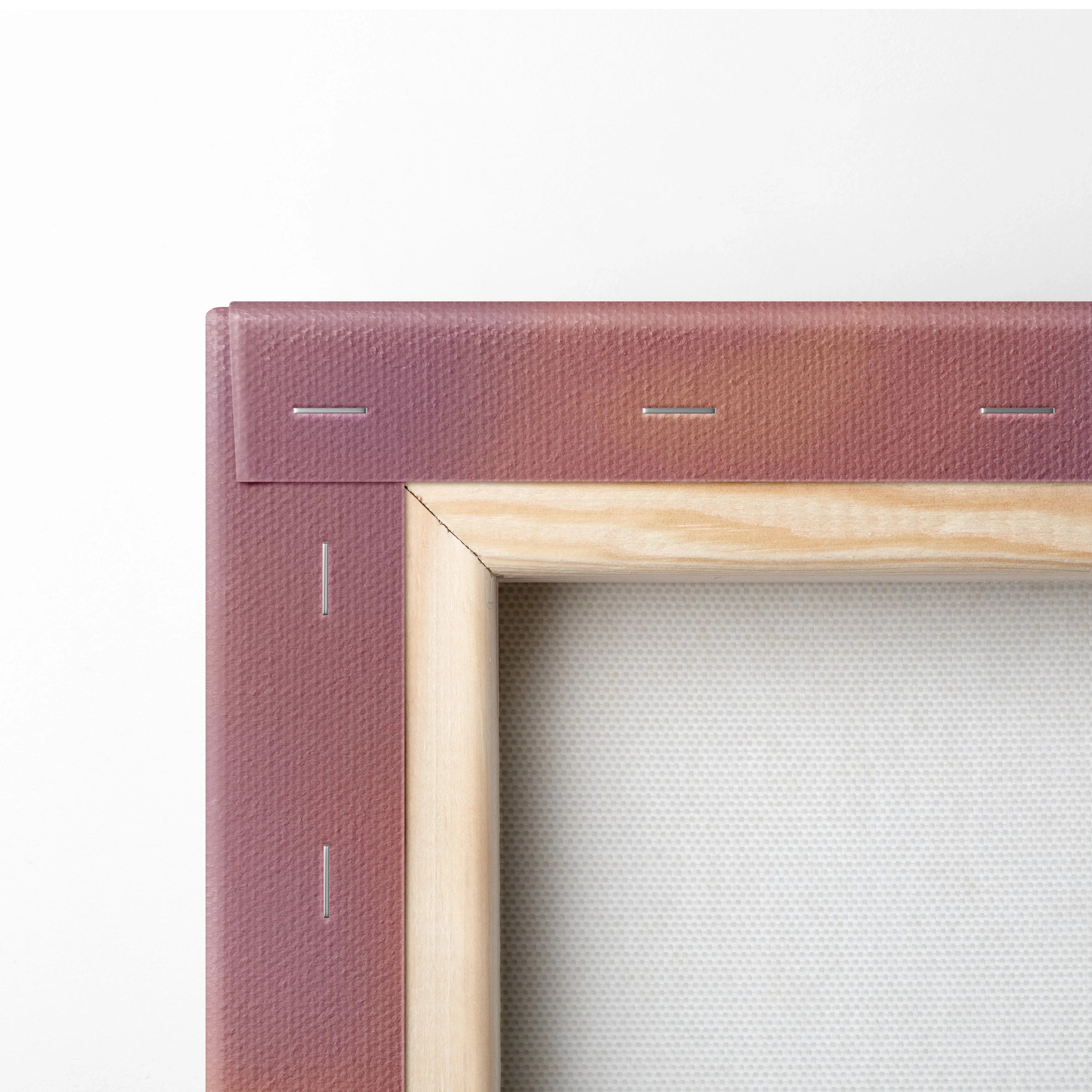 Close-up of a wooden frame and stapled canvas corner with reddish-pink textured backing and plain white canvas surface.