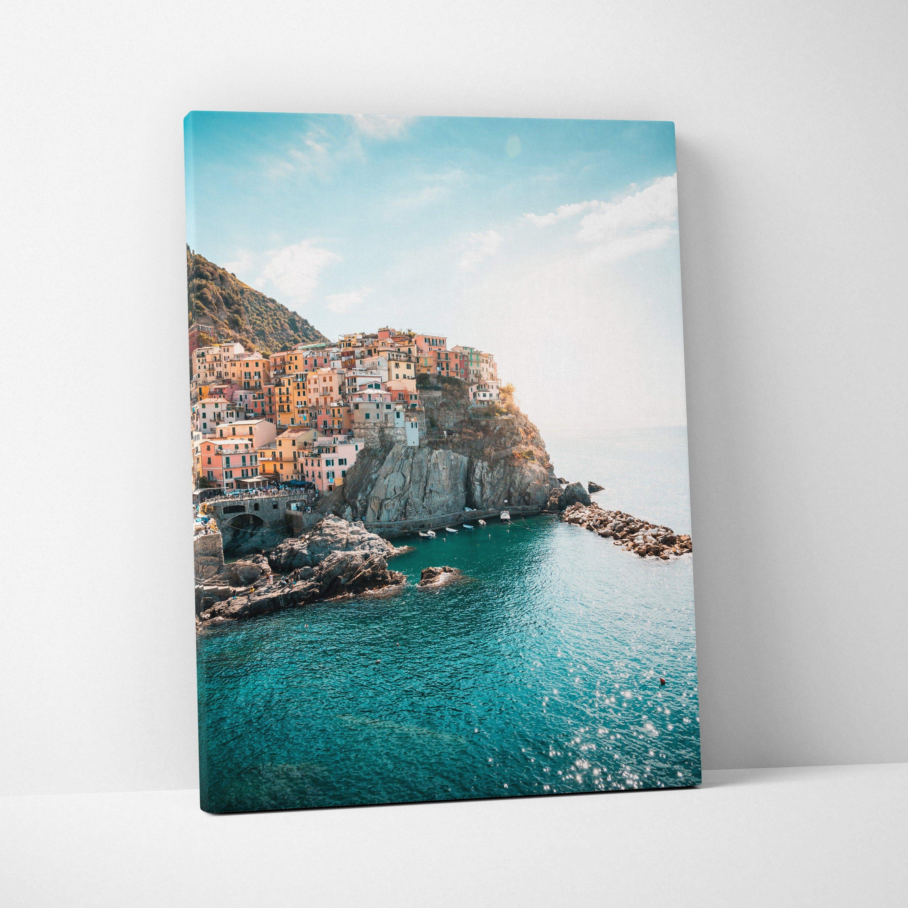 Canvas wall art depicting colorful buildings on cliffs above sparkling turquoise sea under blue sky, inspired by Manarola,.