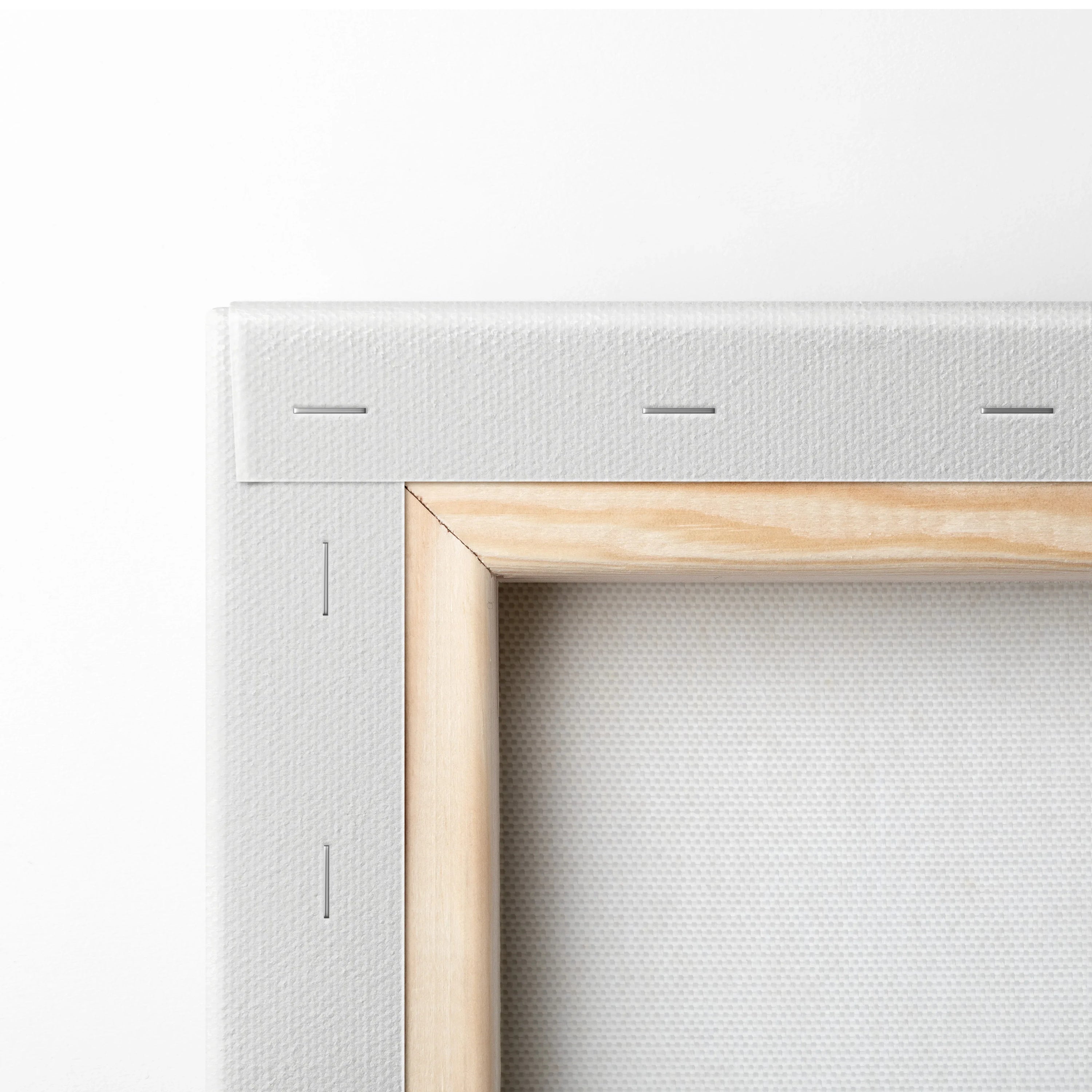 Close-up of stretched white canvas on light wood frame with visible metal staples and textured fabric surface.