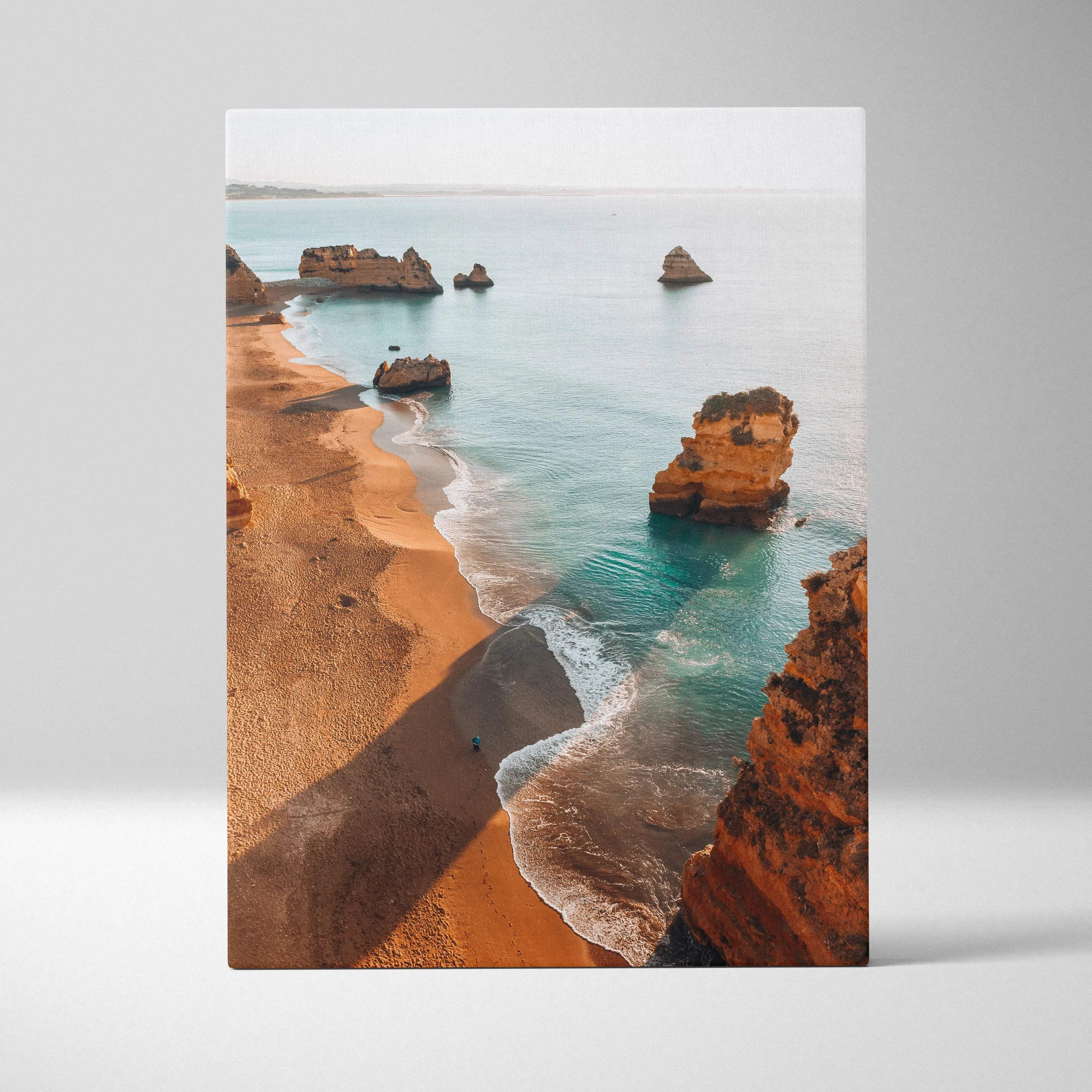 Canvas wall art depicting a sandy beach with large rock formations and calm blue ocean waves.