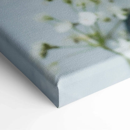Close-up of canvas wall art showing textured fabric and soft, muted floral design with pale greens and whites on a light.