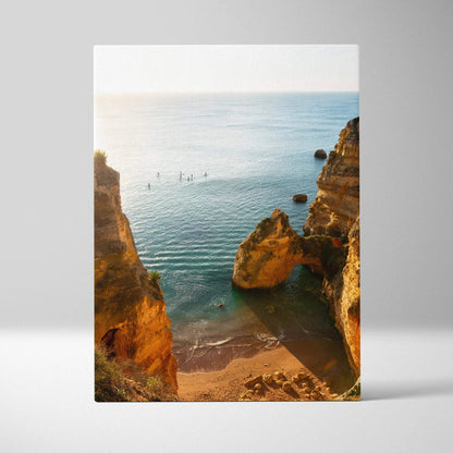 Canvas wall art of a sunlit beach scene with rocky cliffs and calm ocean water.