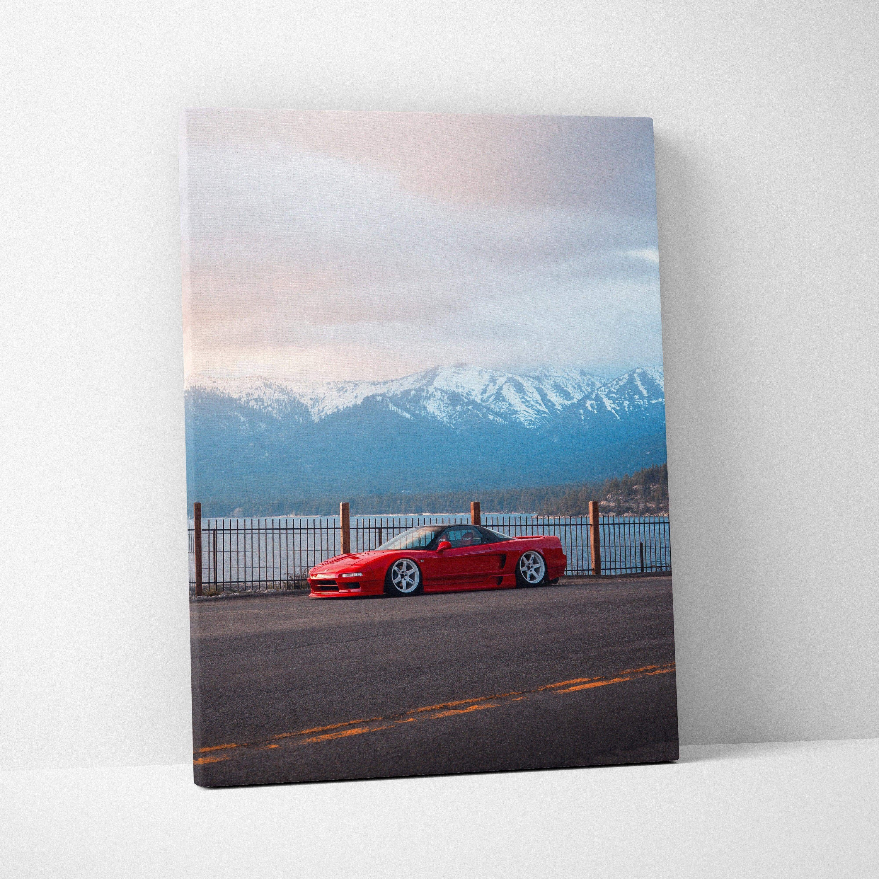 Vertical canvas wall art featuring a red Acura NSX parked by a waterfront with snowy mountains and sunset sky in the.