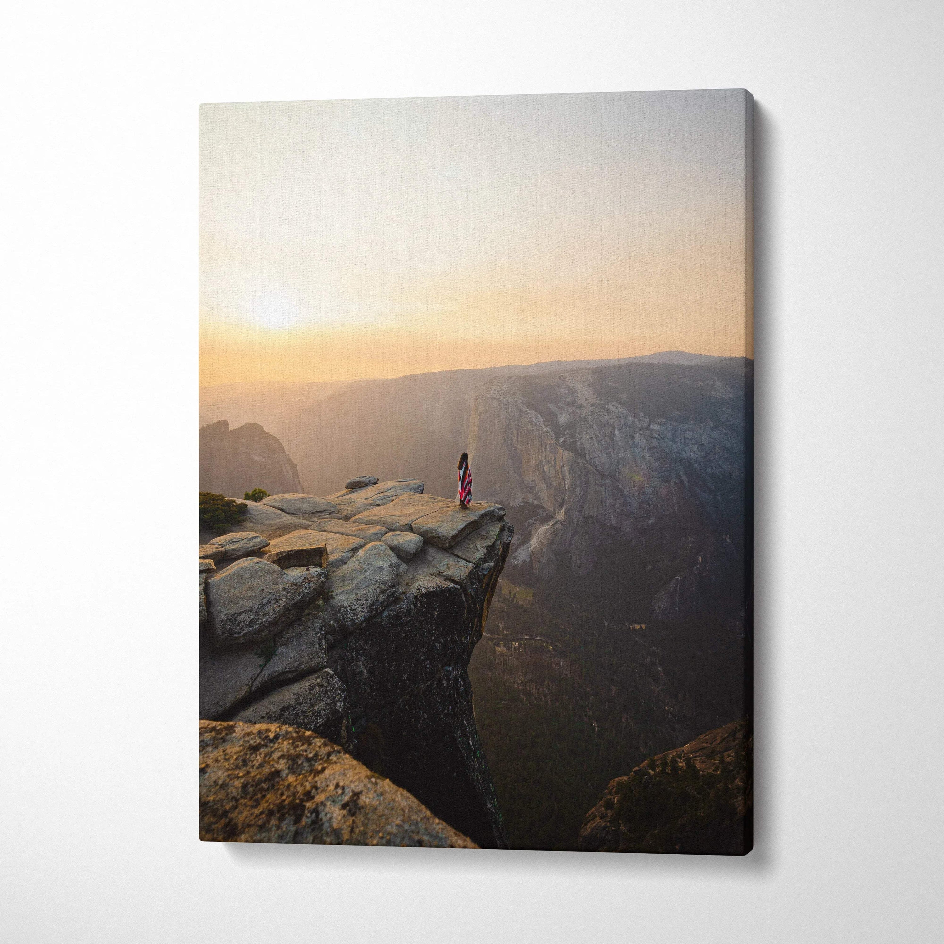 Visionary solitary figure in red striped dress on granite cliff at sunrise over canyon