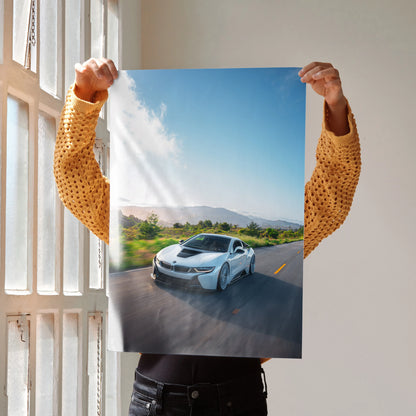 BMW i8 sports car driving on scenic road poster wall art with bright blue sky background.