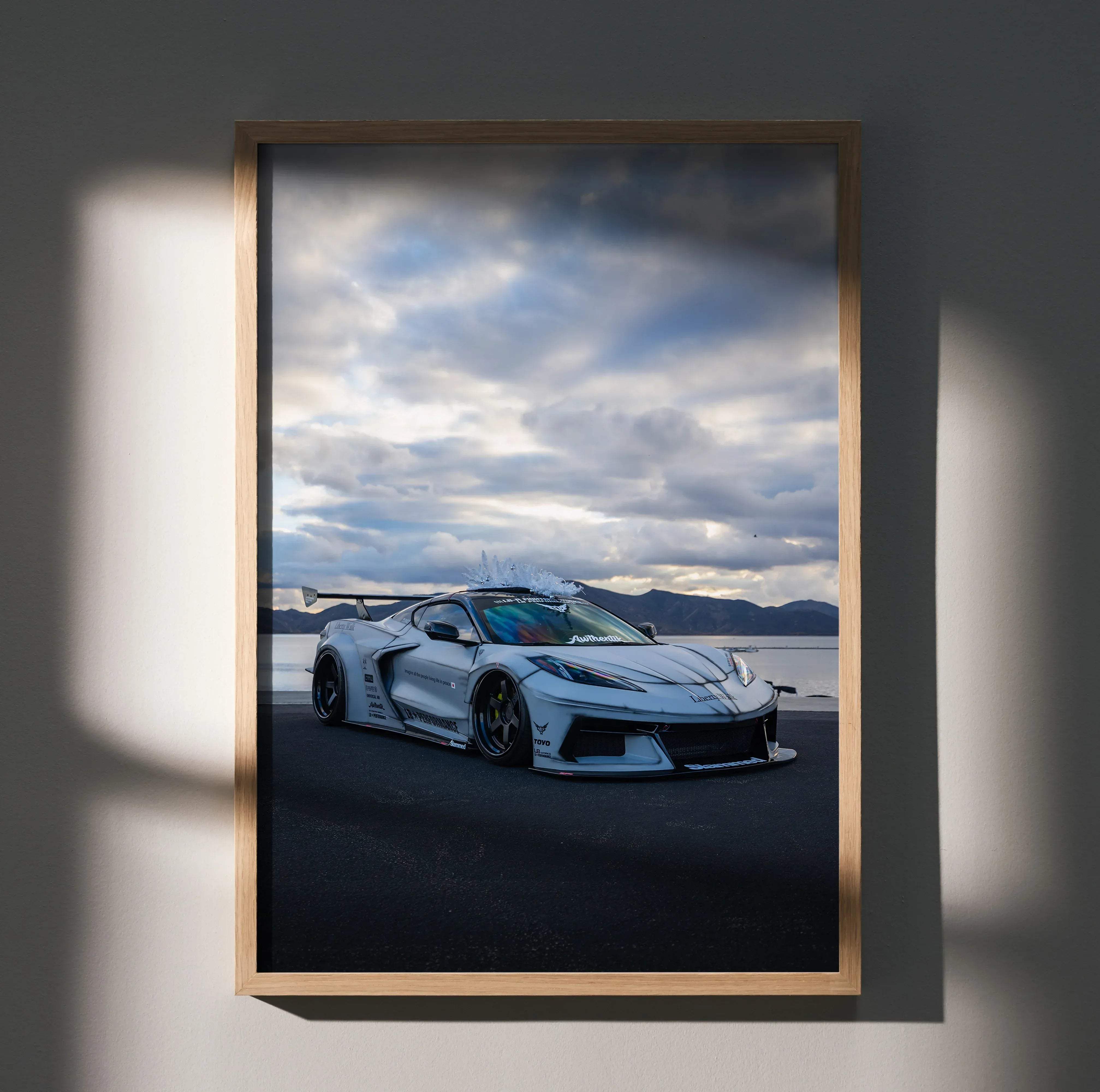 A framed high resolution satin poster of a white custom Chevrolet C8 Corvette with black rims near water under clouds