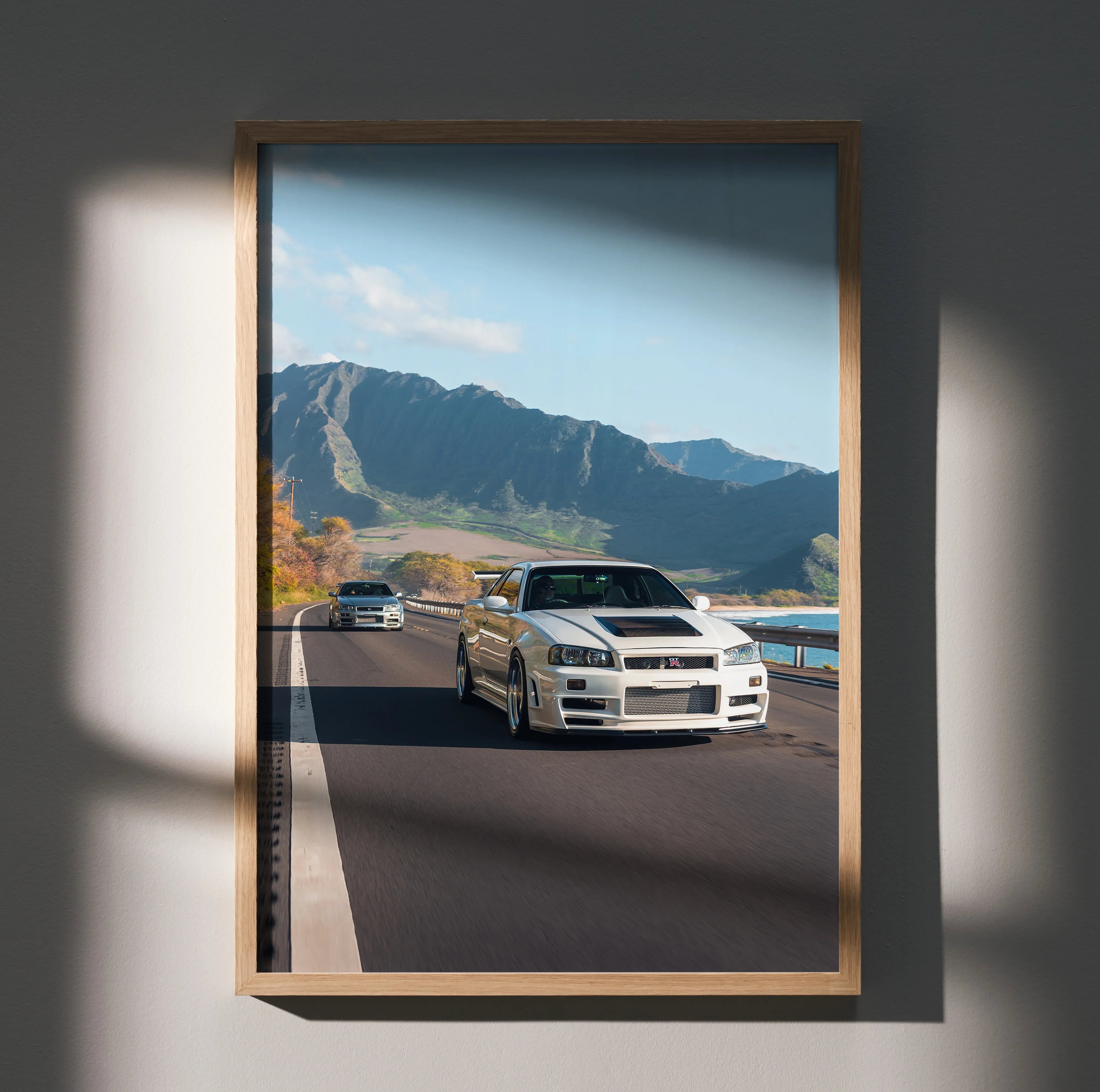 Nissan R34 GT-R driving on scenic mountain road poster wall art in wooden frame.