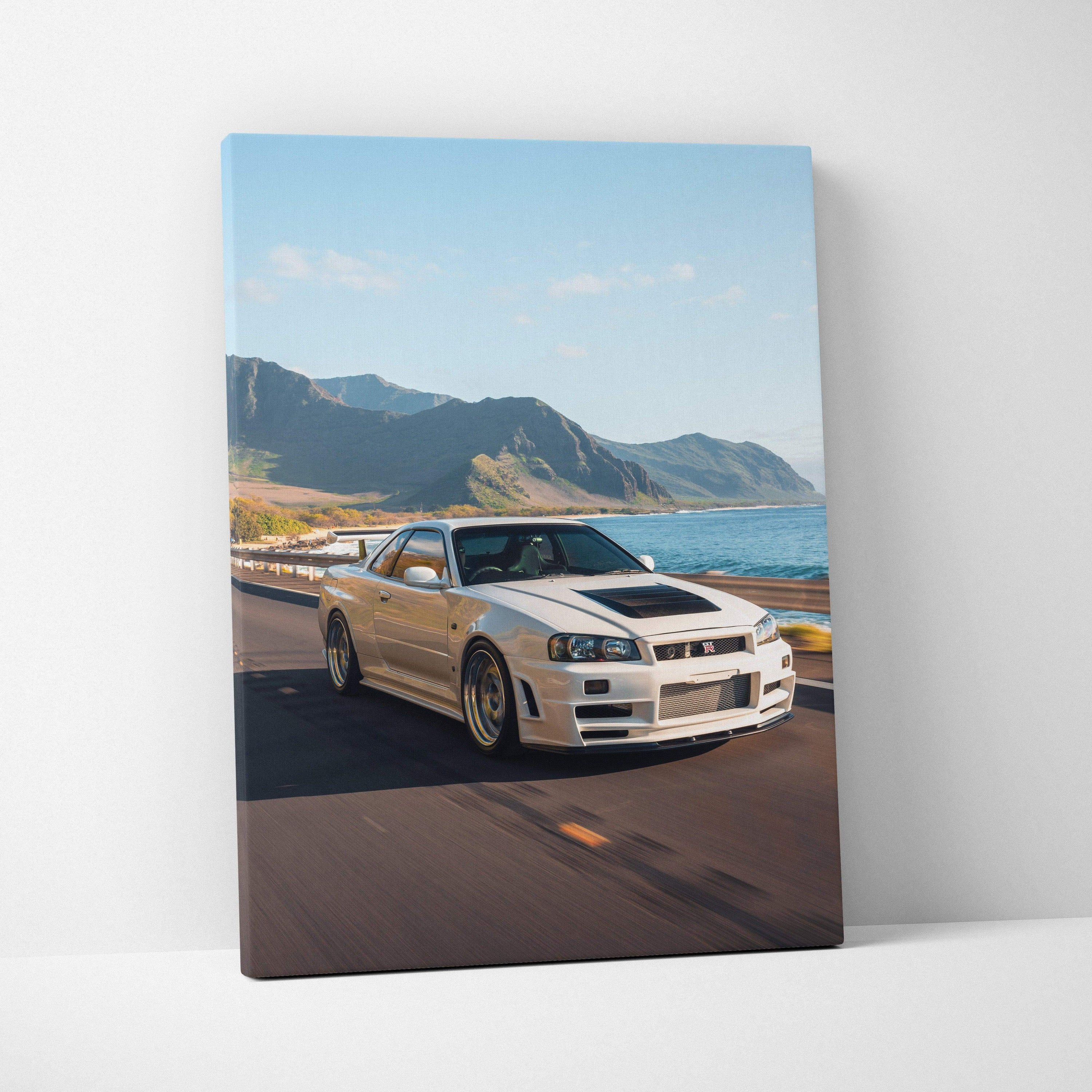 Nissan R34 GTR driving on coastal road canvas wall art with mountains and ocean backdrop.
