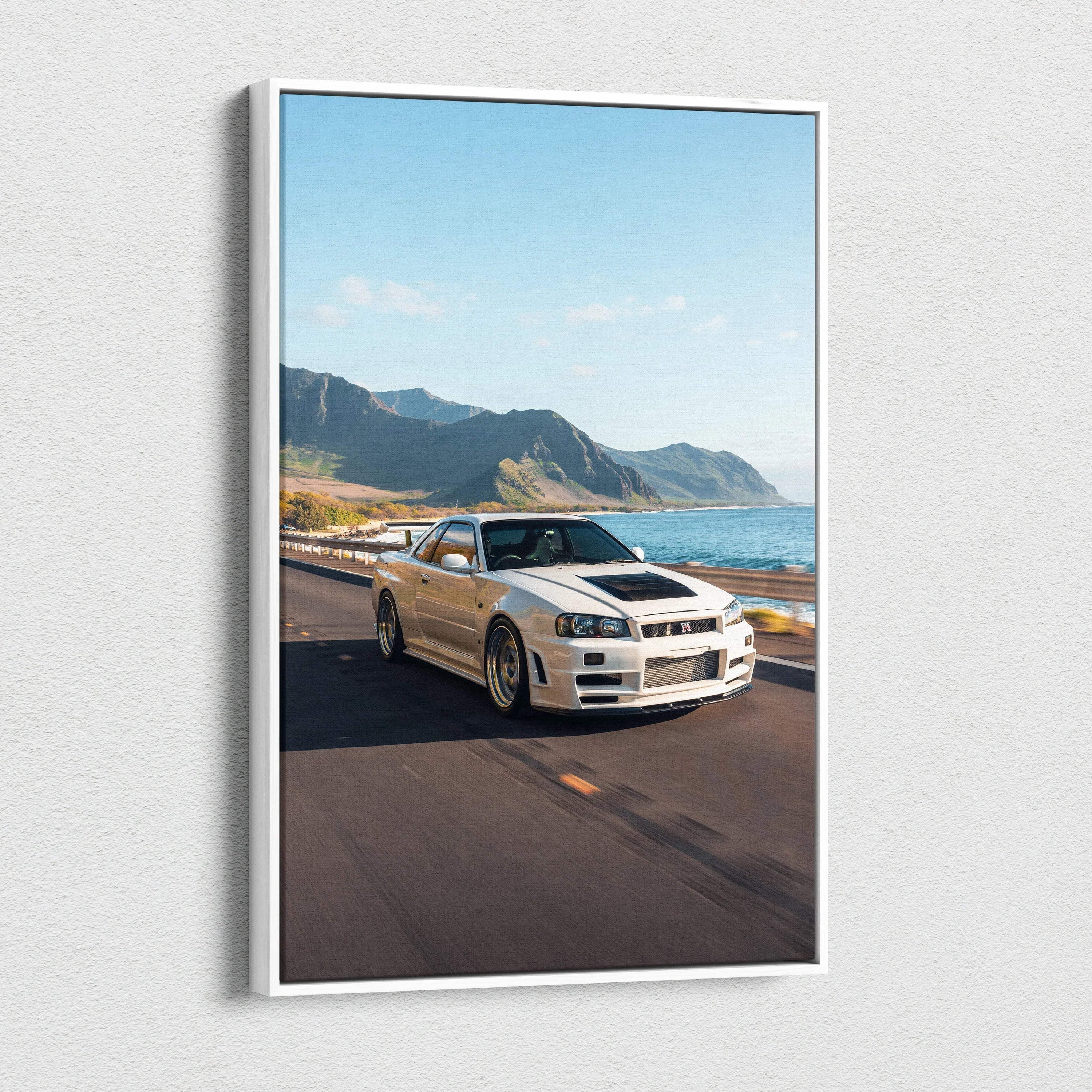Vertical canvas wall art featuring a white Nissan R34 GTR Skyline on a coastal road with mountains and ocean backdrop.