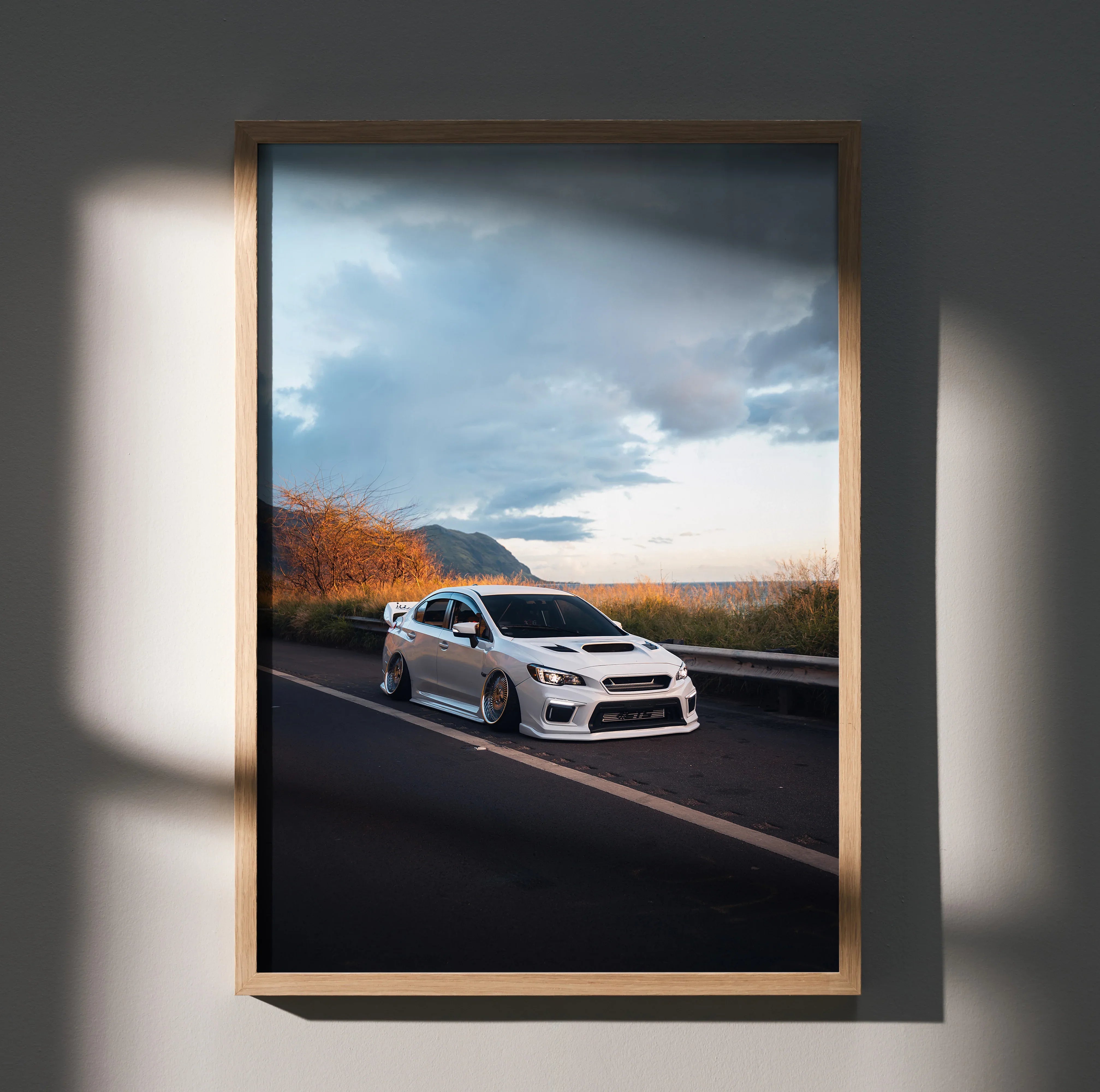 Slammed white Subaru WRX on road under moody sky poster wall art in wooden frame.