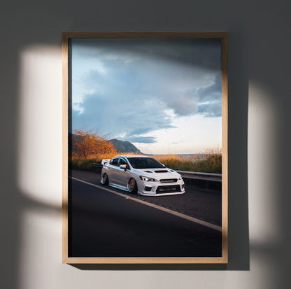 Slammed white Subaru WRX on road under moody sky poster wall art in wooden frame.