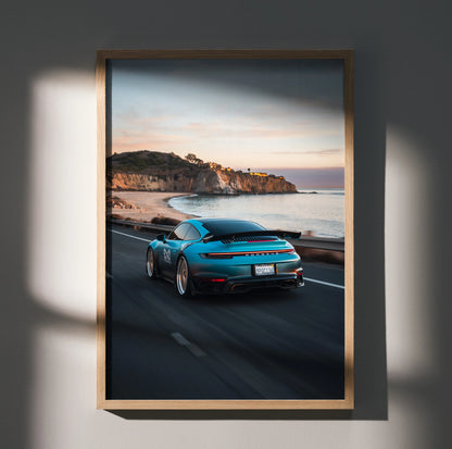 Porsche 911 driving on coastal road at sunset poster wall art in wooden frame.