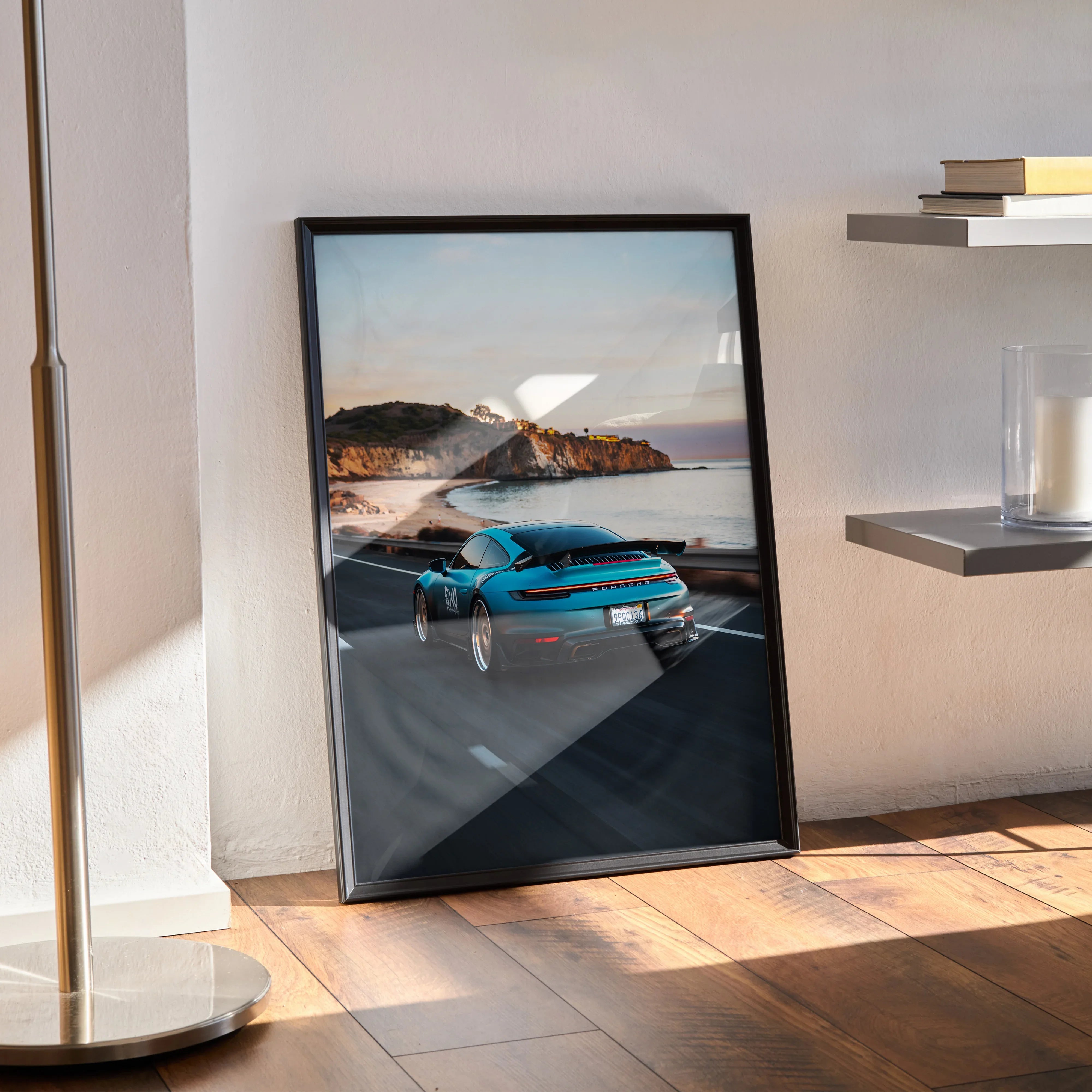 Porsche 911 blue sports car poster leaning against wall with coastal background wall art.