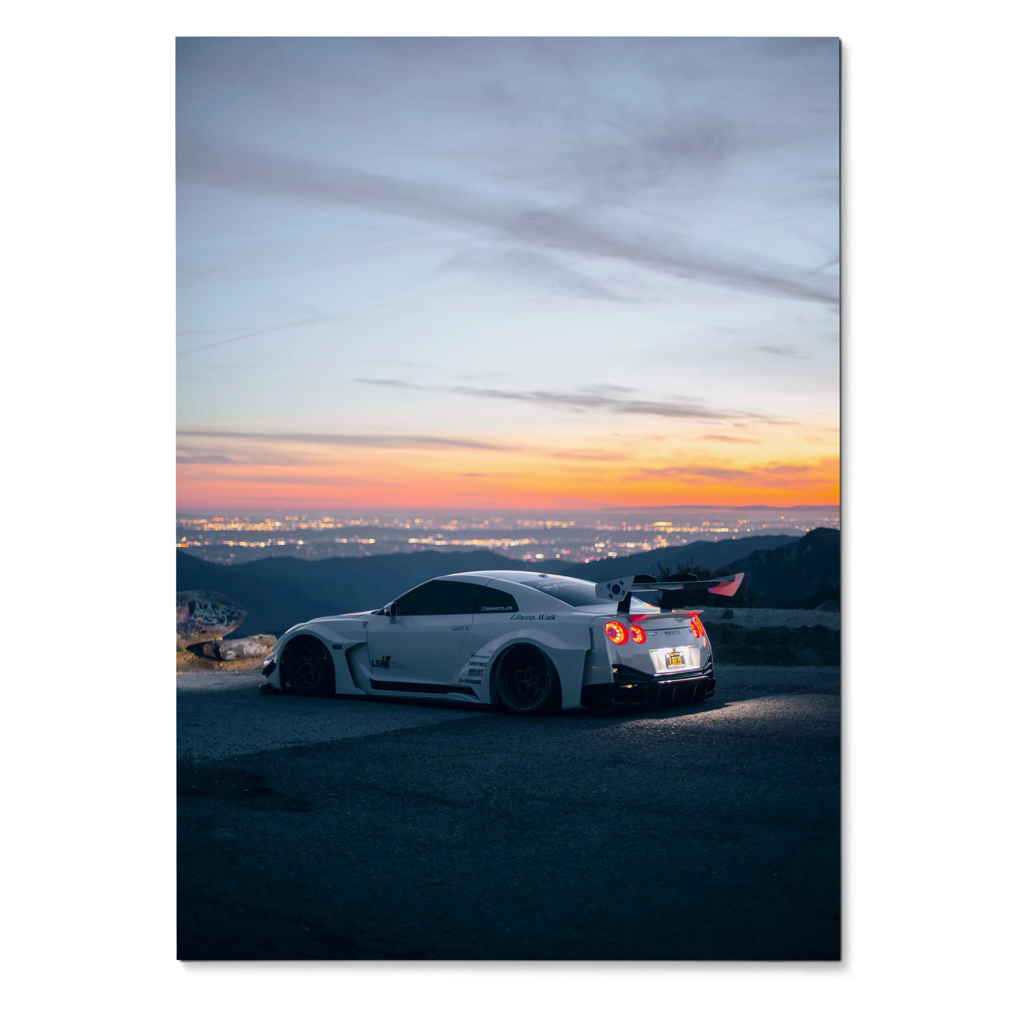 Nissan R35 GT-R parked on hilltop at sunset with city lights in background wall art poster.