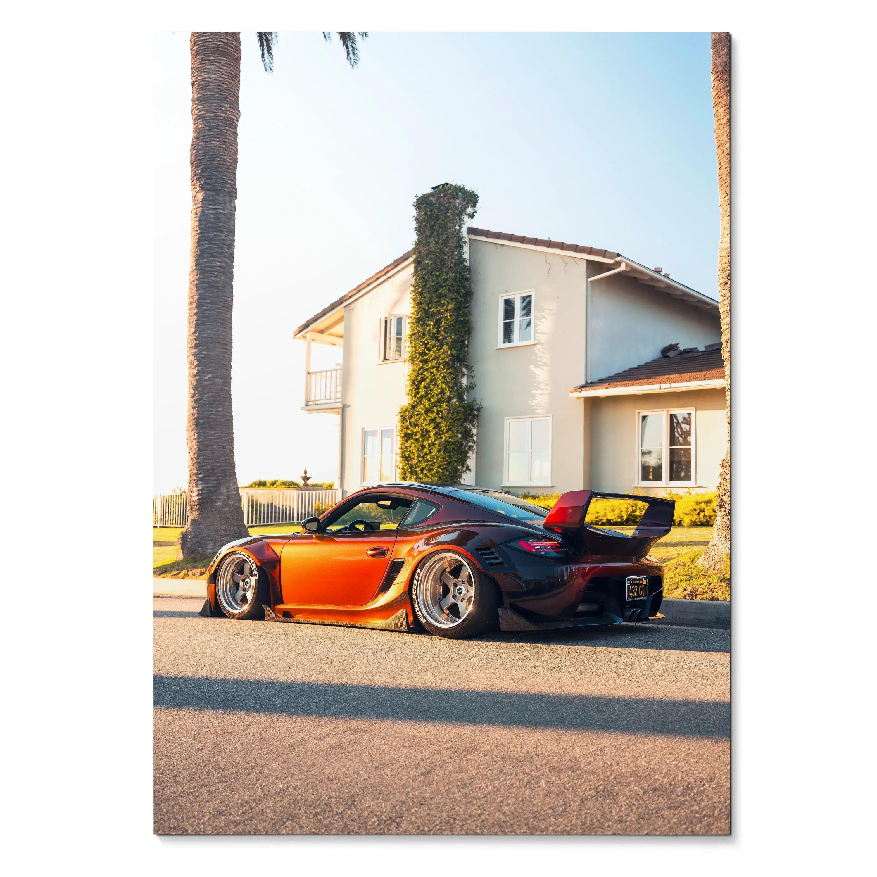 Porsche Cayman in vibrant orange with black accents parked in front of a sunlit house poster wall art.