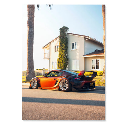 Porsche Cayman in vibrant orange with black accents parked in front of a sunlit house poster wall art.