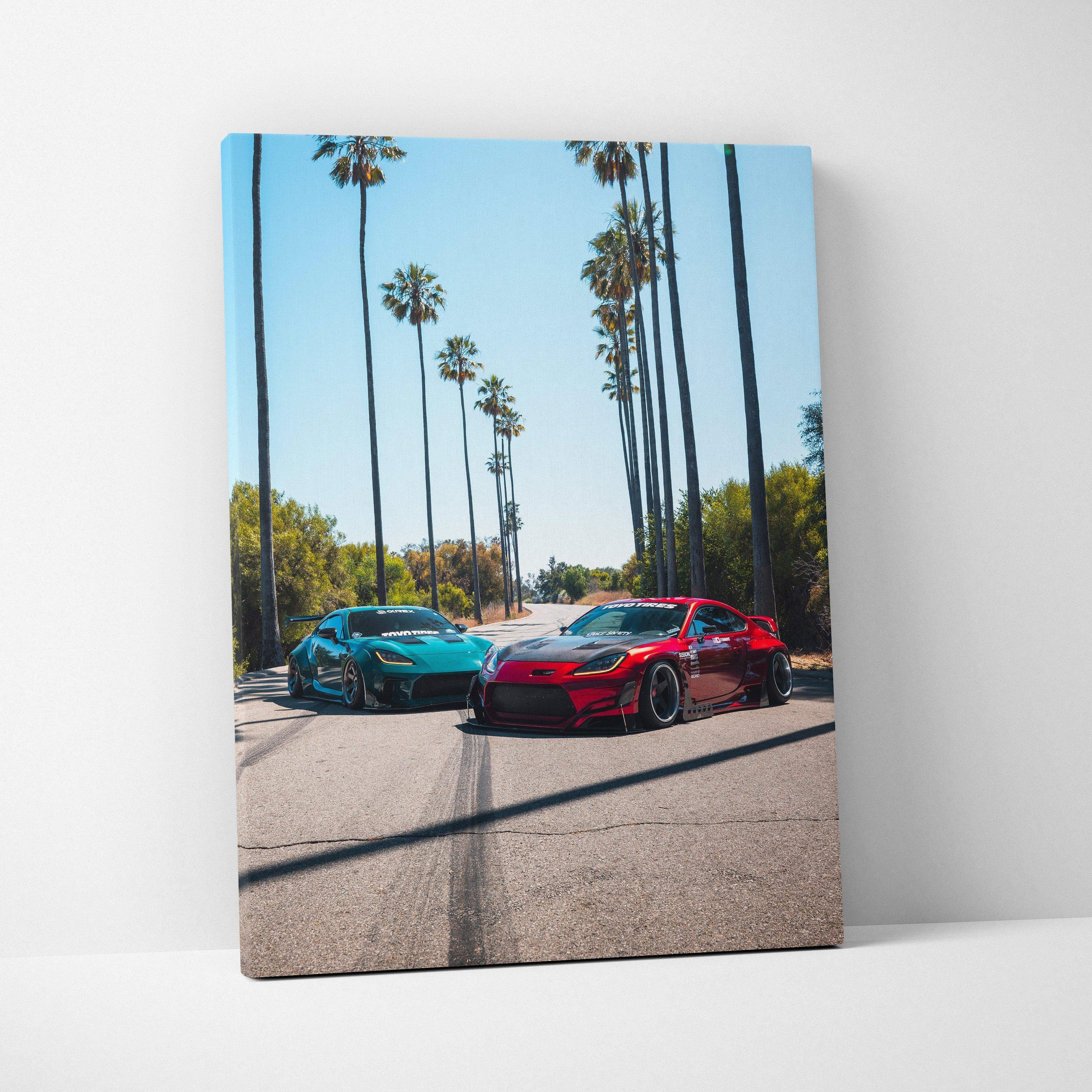 Vertical canvas wall art featuring vibrant red and teal Toyota GR86 cars on a sunny palm-lined street.