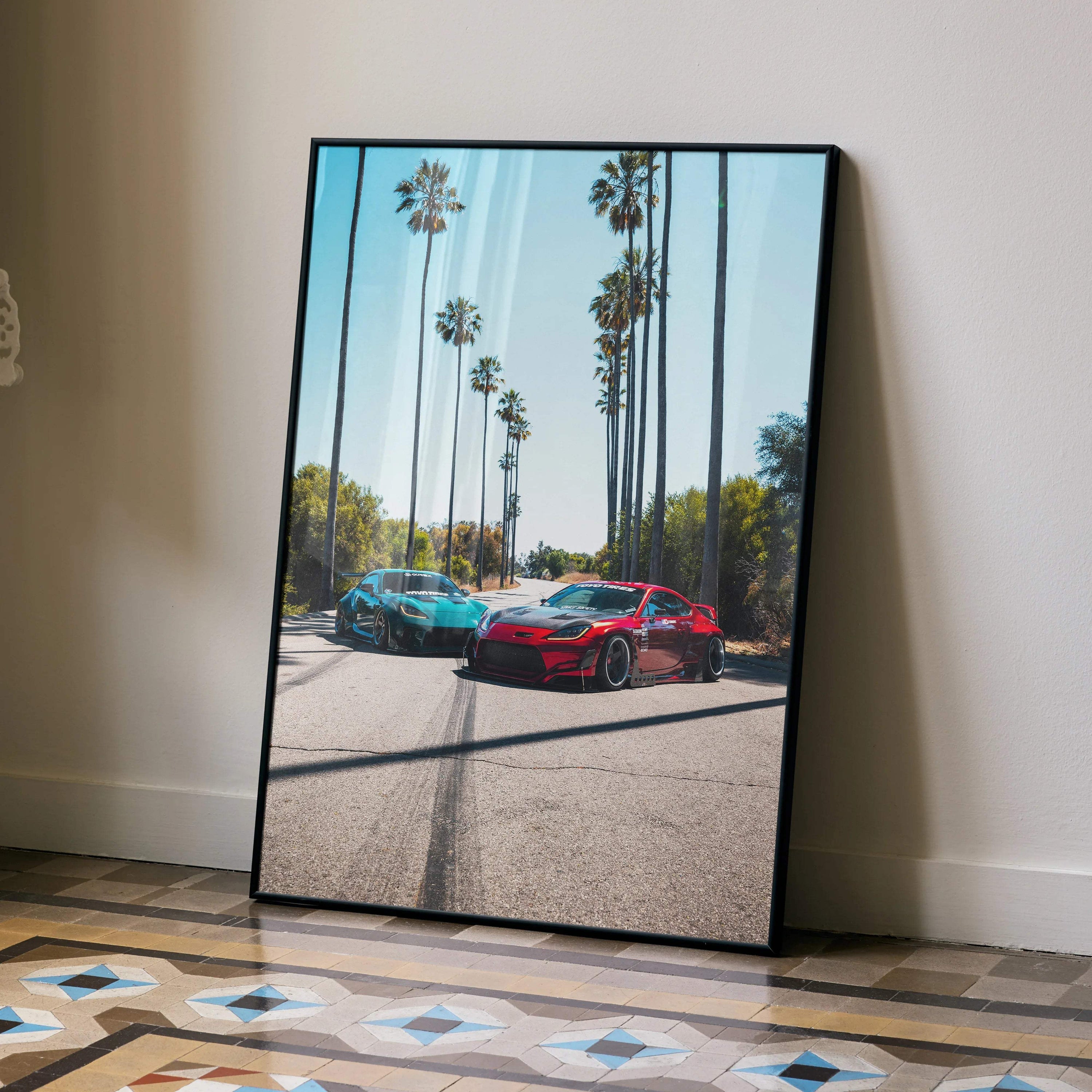 Toyota GR86 and FRS cars on palm-lined street framed as wall art poster leaning on floor.