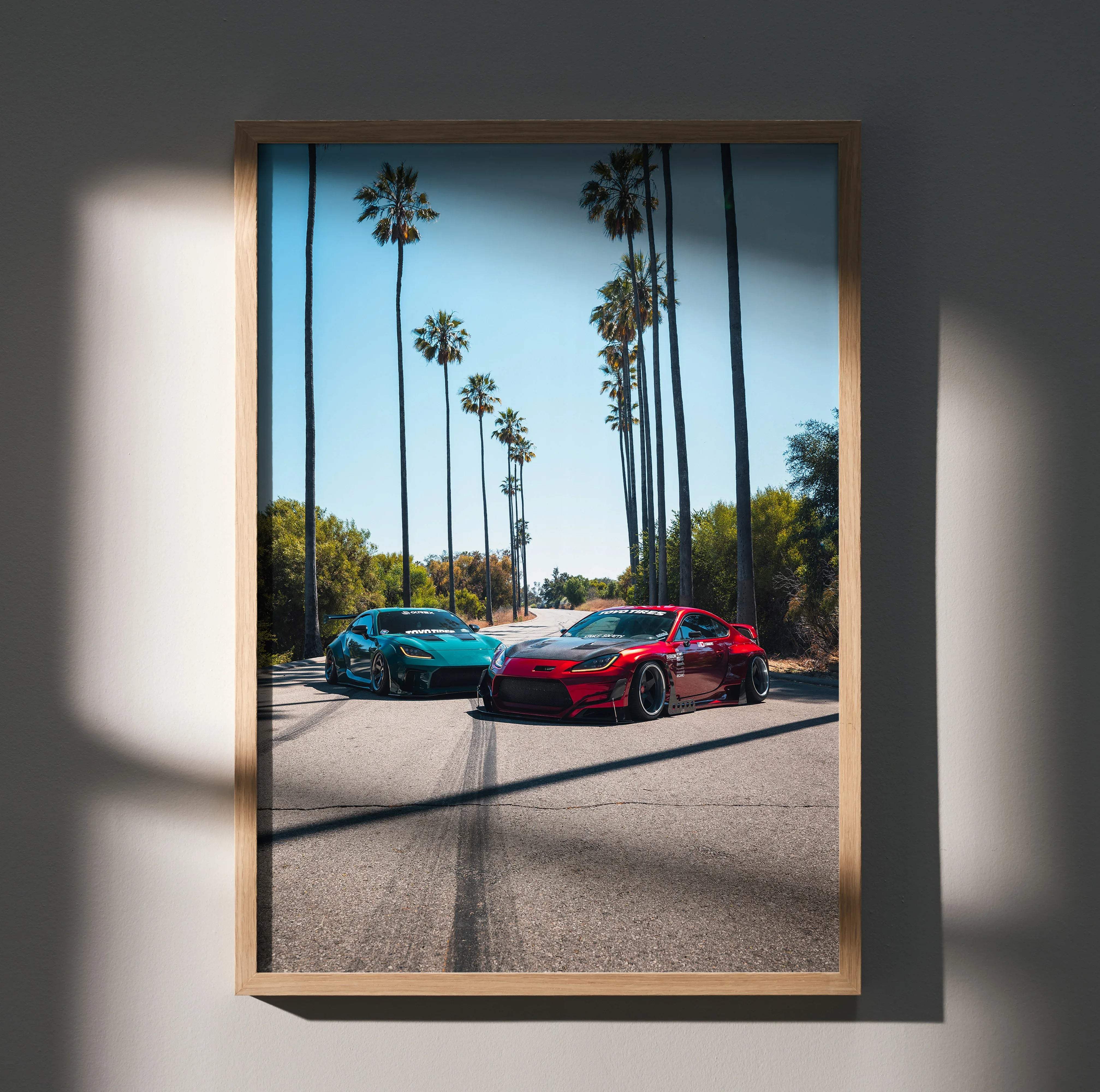 A framed high resolution Toyota GR86 wall art poster featuring teal and red sports cars on a palm lined road