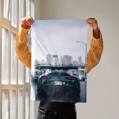 Toyota Supra Mk5 black rear view poster held up as wall art with city skyline background.