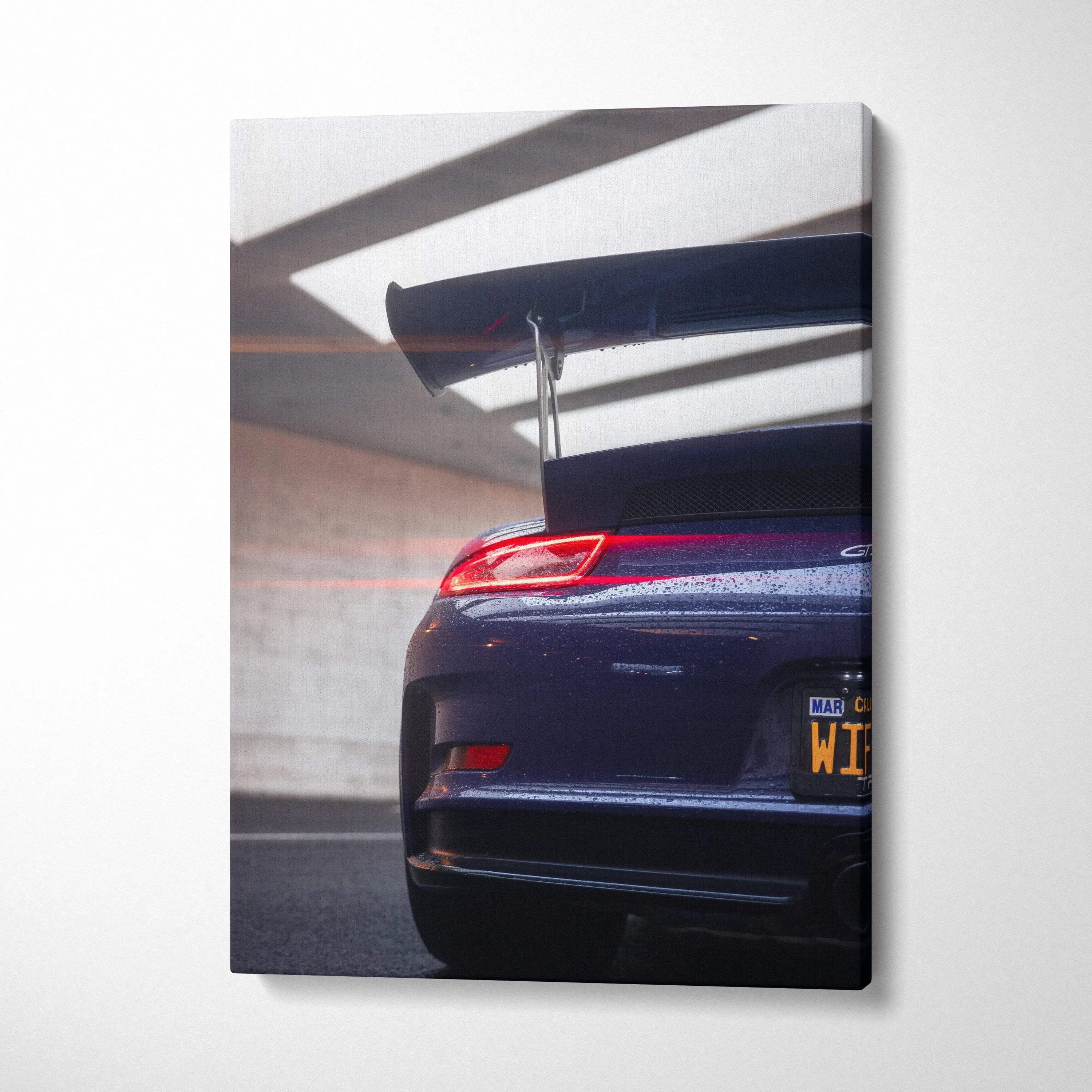 Vertical canvas wall art featuring the rear end and spoiler of a dark blue Porsche 911 GT3 RS in a garage.