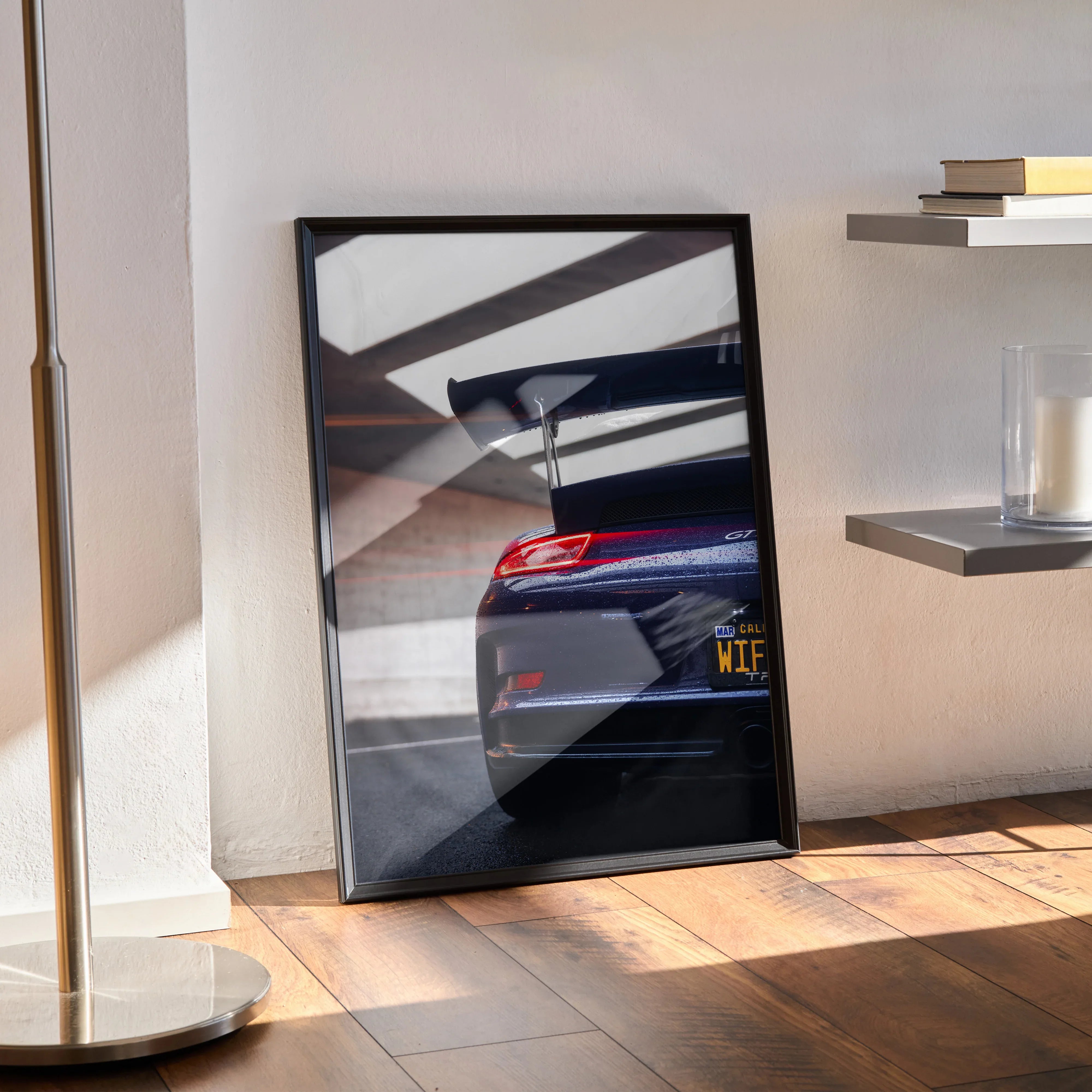 Porsche 911 GT3 RS rear view poster wall art with black frame leaning on floor near shelves.
