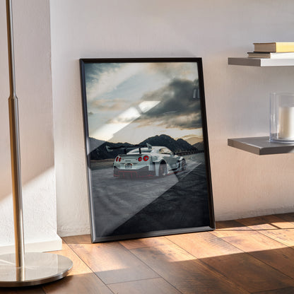 Nissan GTR R35 poster wall art with mountain background in black frame on wood floor.