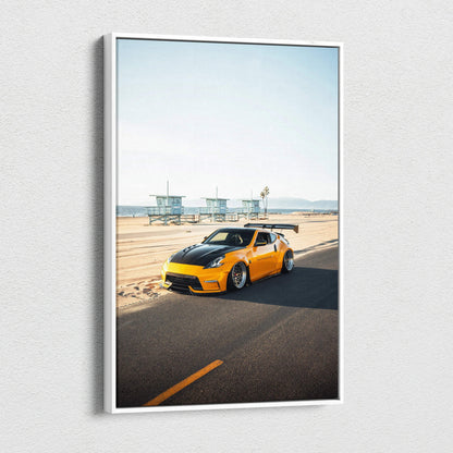 Vertical canvas wall art of a yellow Nissan 370z on a sunny coastal road with lifeguard towers in the background.
