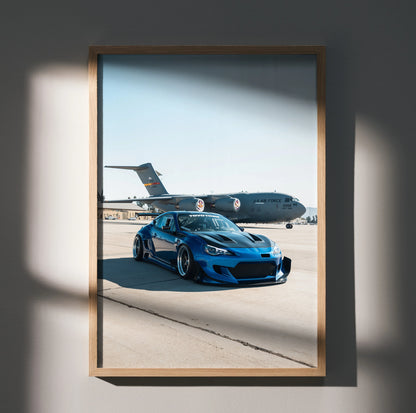 Sleek blue widebody Toyota FRS parked on runway with military plane background poster wall art.