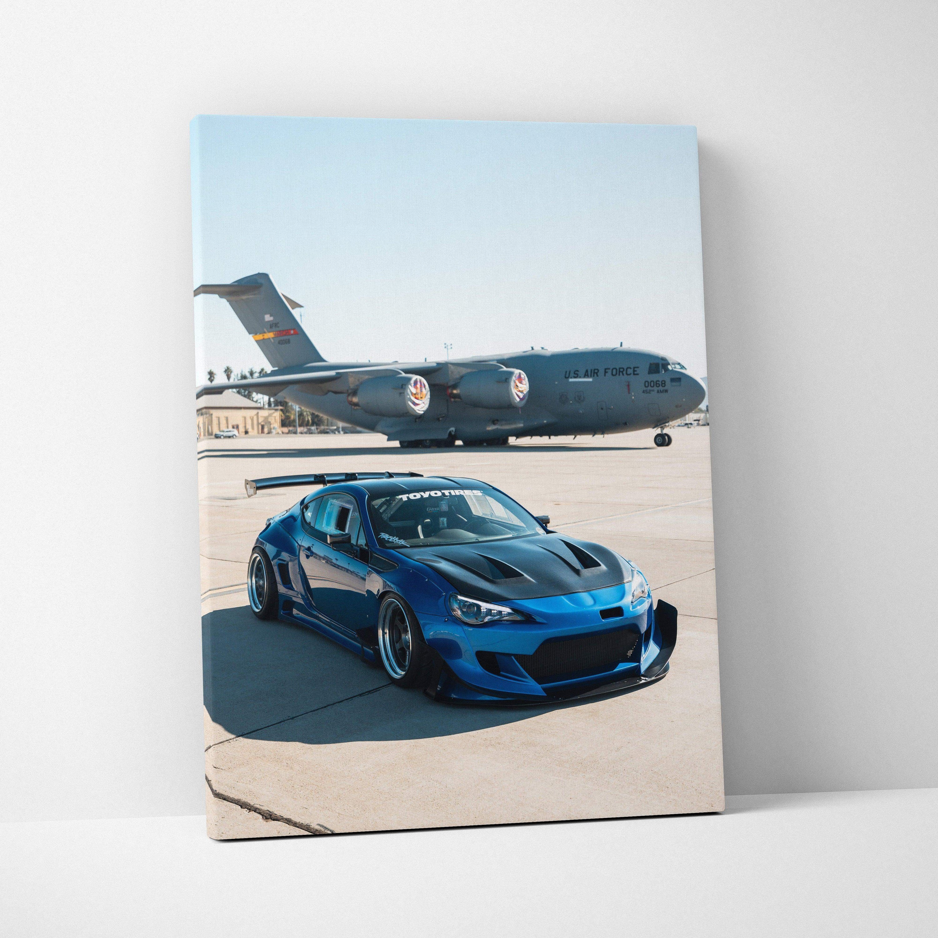 Blue Toyota FRS parked on runway with military cargo plane in background vertical canvas wall art.