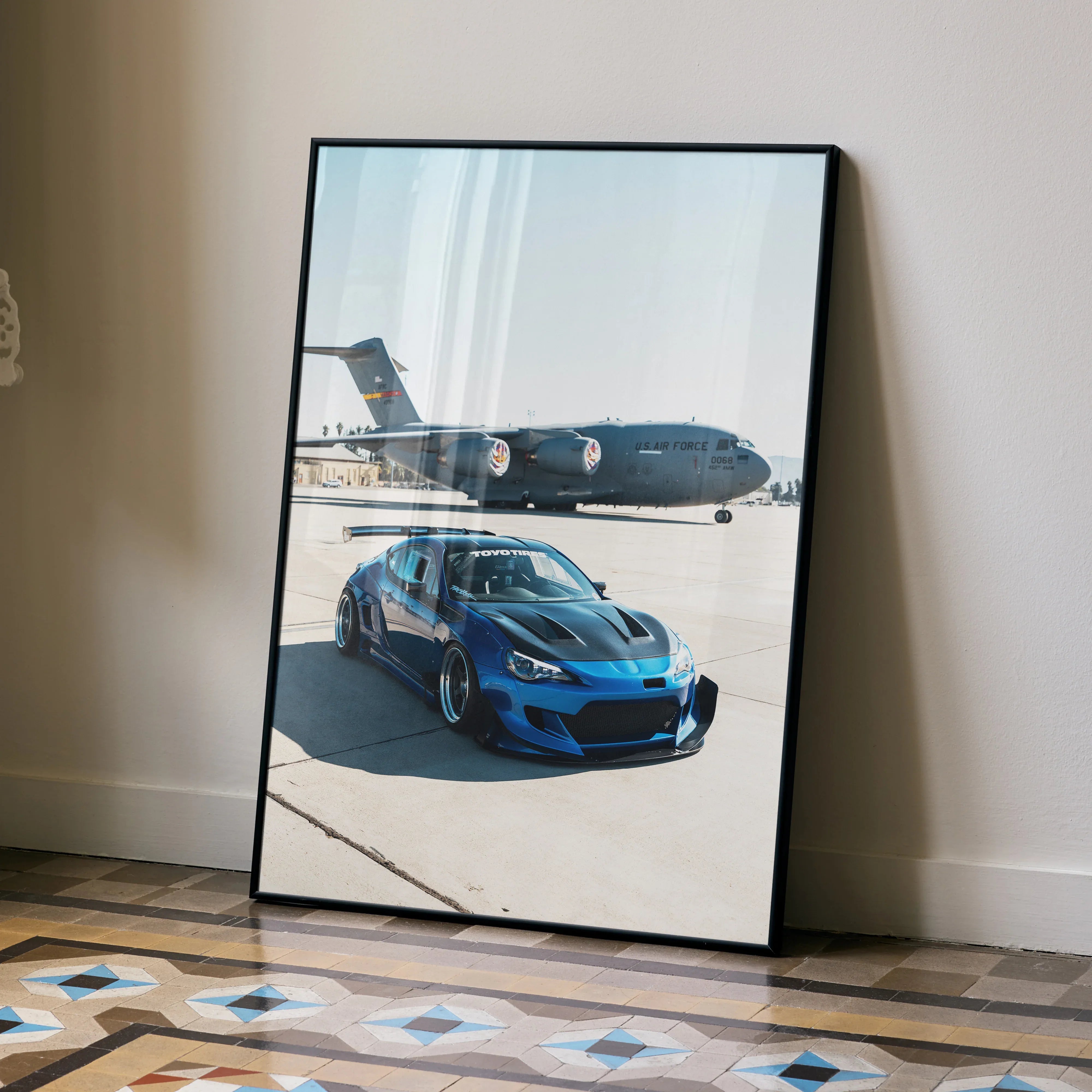 Blue Toyota FRS poster leaning on wall, automotive wall art with jet in background.
