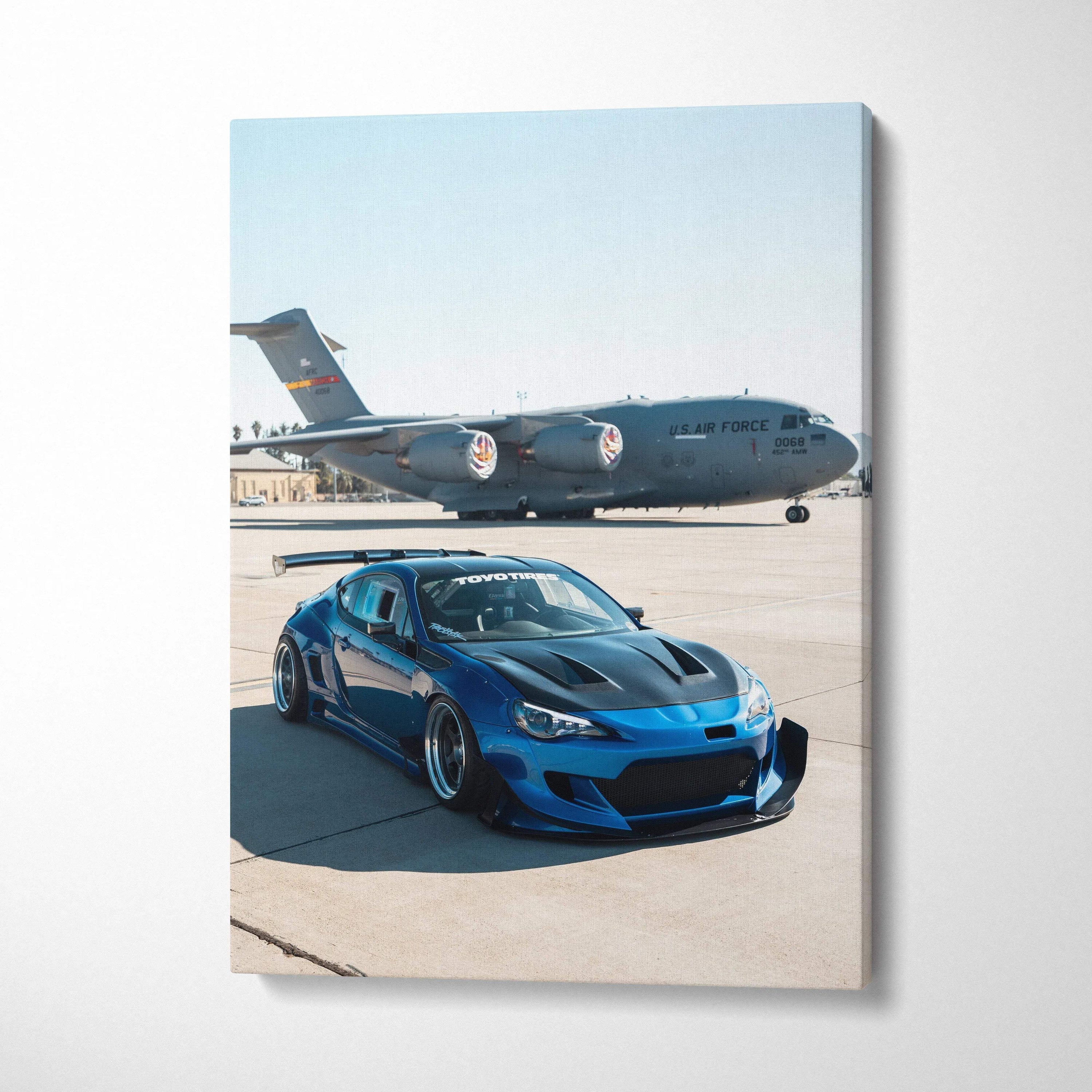 Blue Toyota FRS parked on runway with military cargo plane in background vertical canvas wall art.