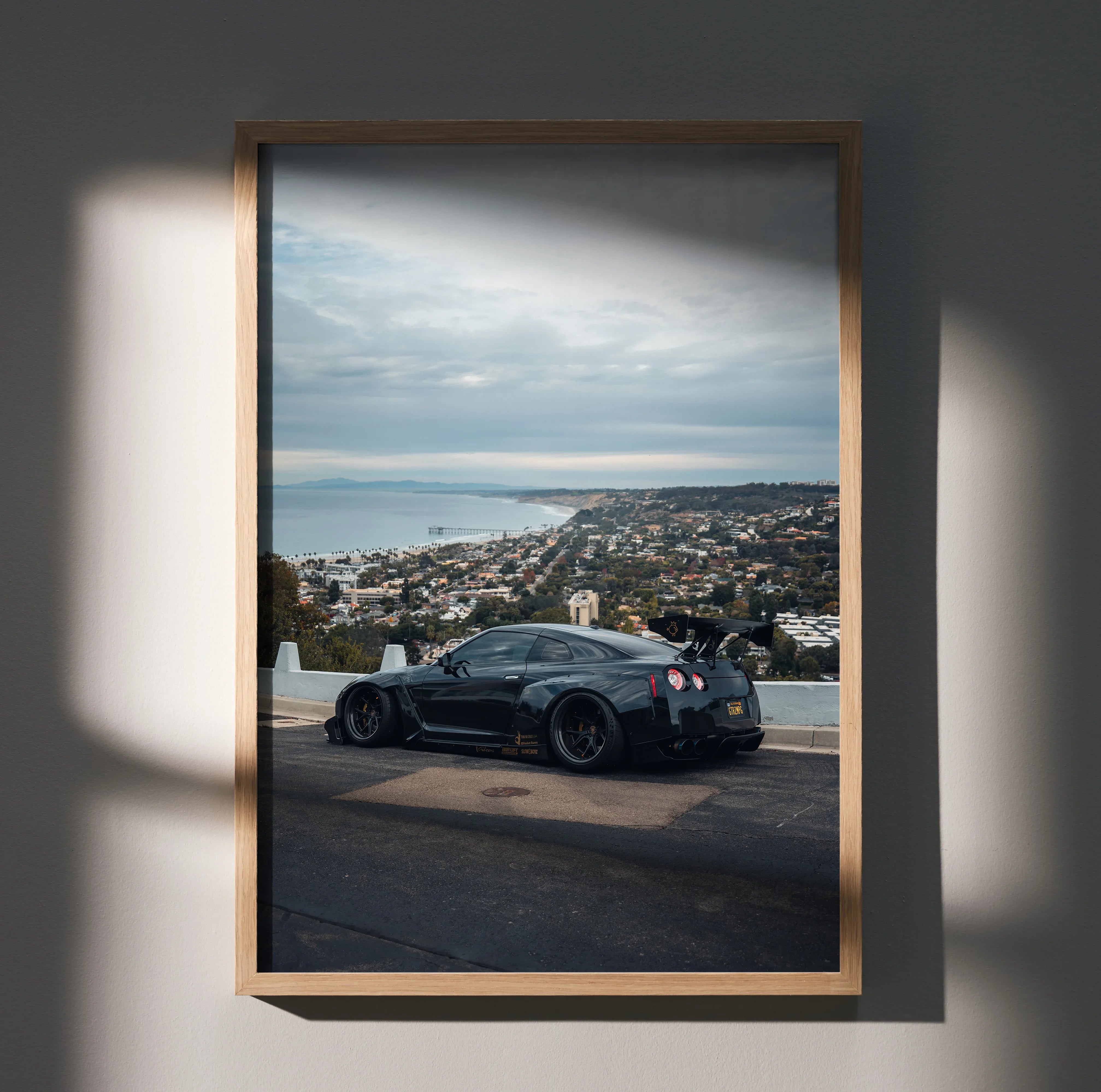Nissan R35 GTR black sports car on coastal road poster wall art in wooden frame.
